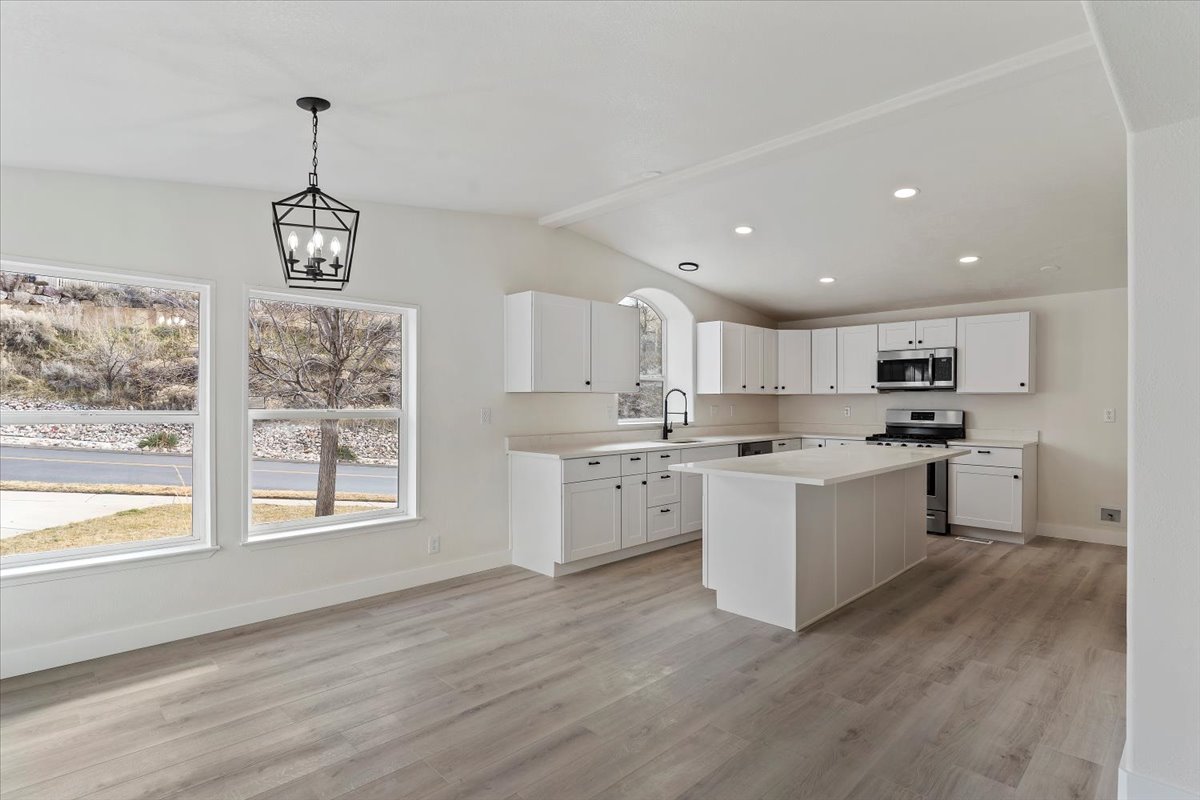 Open-concept kitchen and dining area featuring light wood-finish flooring, white cabinetry, a central island, stainless steel appliances, and a modern black chandelier