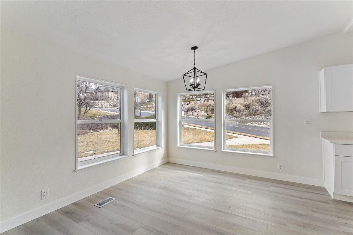 Bright interior space featuring multiple windows, wood-finish flooring, a contemporary black geometric chandelier, white walls, and built-in white cabinetry