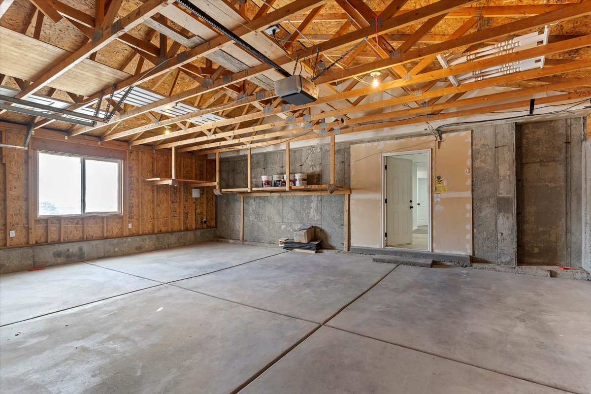 Spacious garage with exposed wooden ceiling trusses, a concrete floor, and integrated shelving