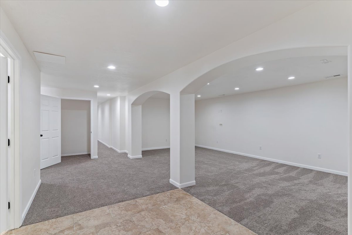 Spacious interior featuring neutral carpeting, arched doorways, white walls, recessed lighting, and a neutral tile floor entrance