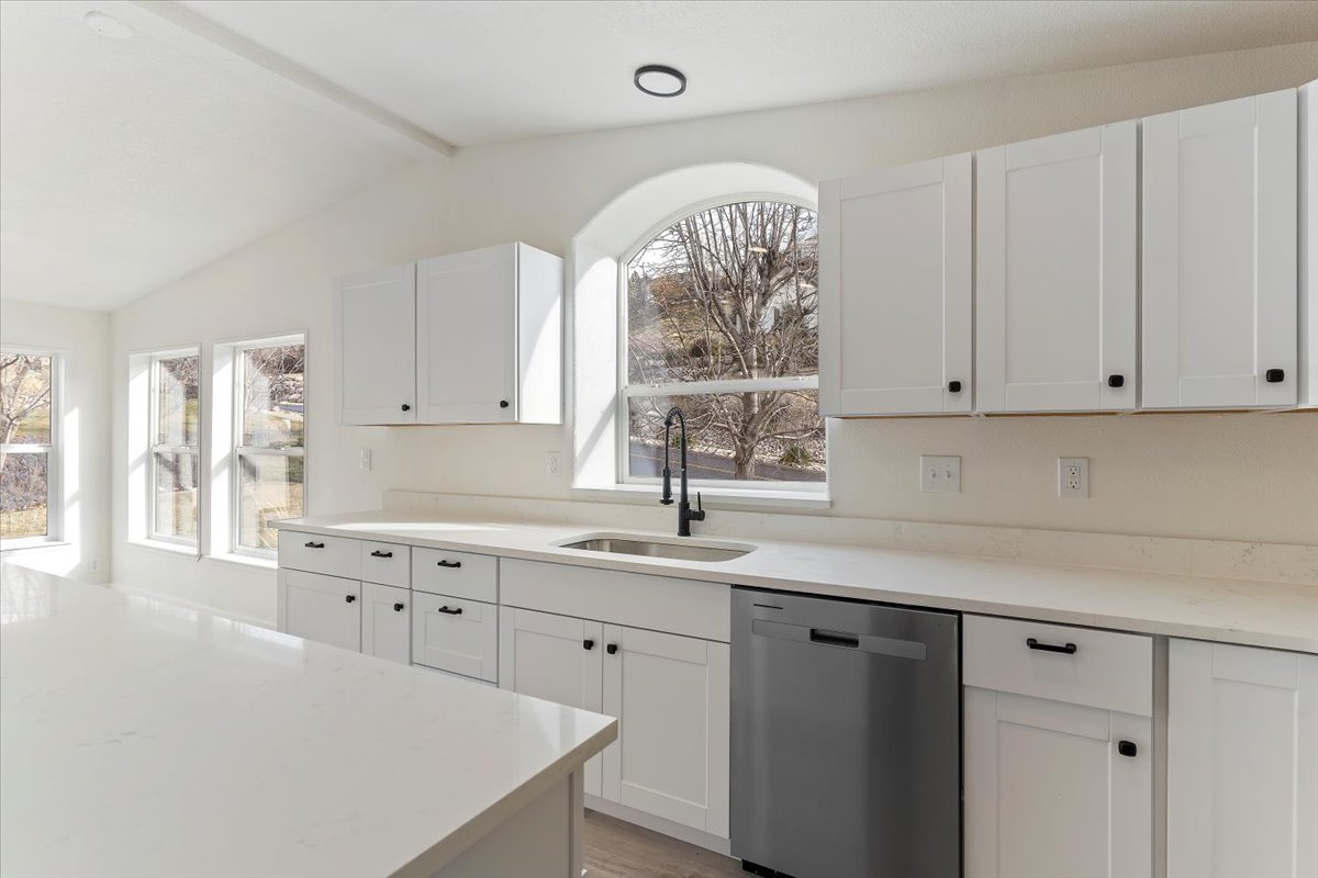 Bright kitchen with white cabinetry, light countertops, stainless steel dishwasher, and a black faucet at the sink