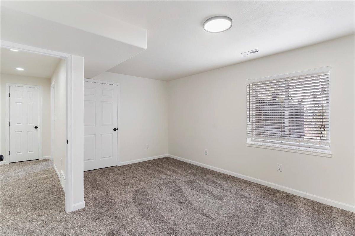 Spacious room featuring gray patterned carpeting, a single window with blinds, and a flush-mount ceiling light