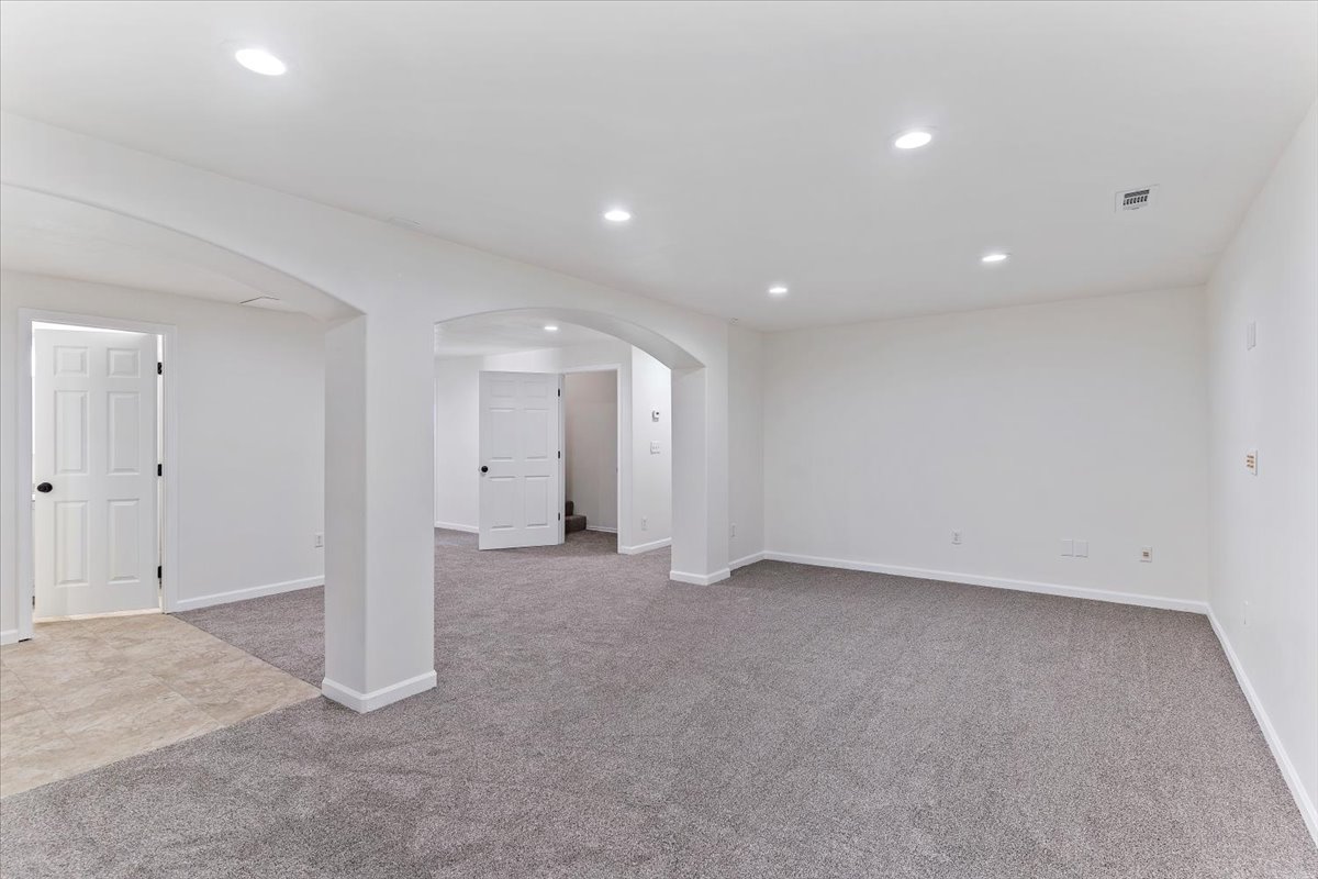 Spacious room featuring neutral carpeting, white walls, recessed lighting, and architectural archways