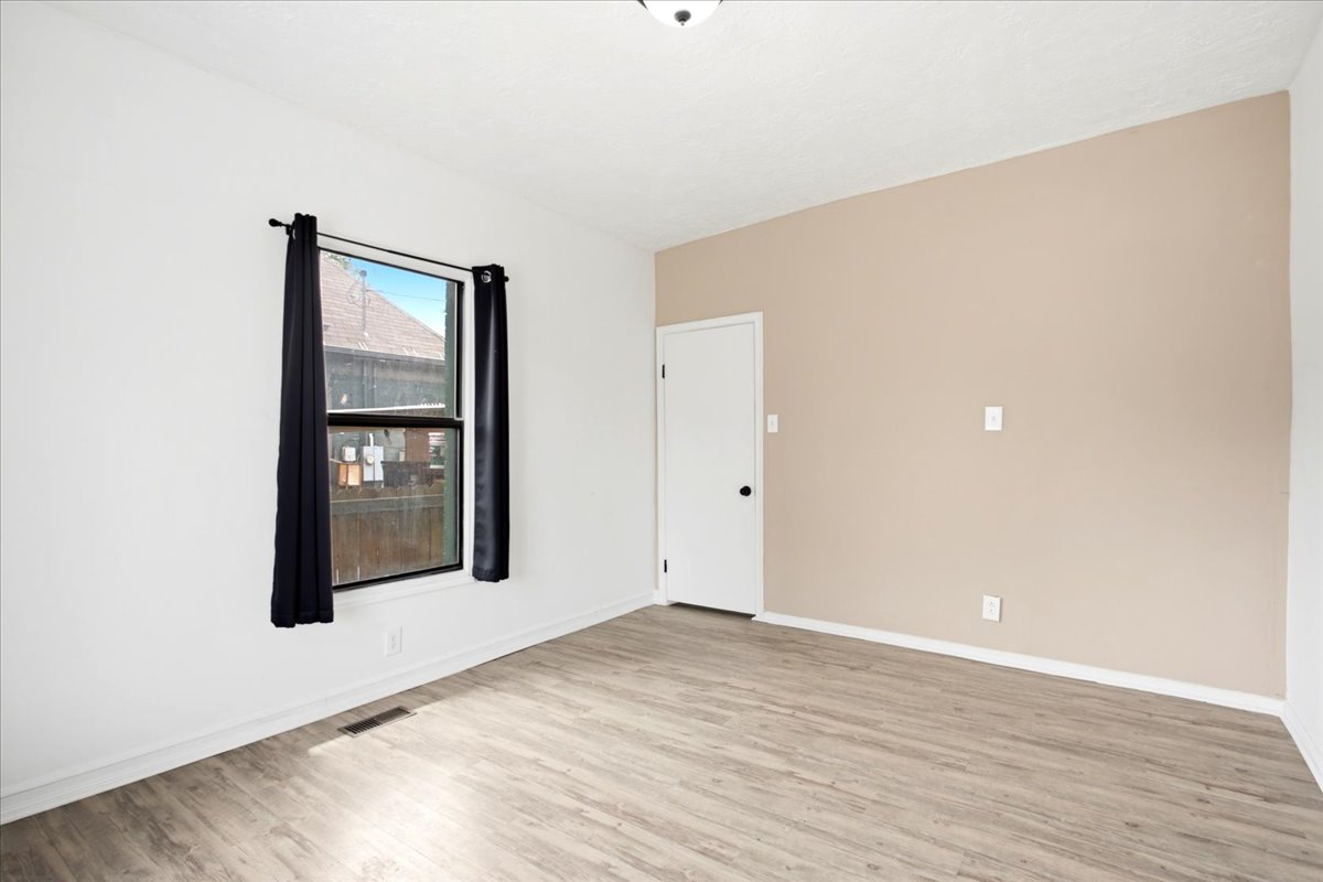 Spacious room featuring wood-finish flooring, a light neutral accent wall, and a white door with black hardware
