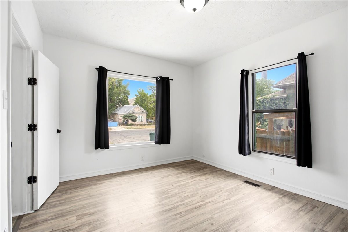 Room featuring wood-finish flooring, two windows with dark curtain rods and curtains, white baseboards, and a white ceiling with a flush-mount light fixture