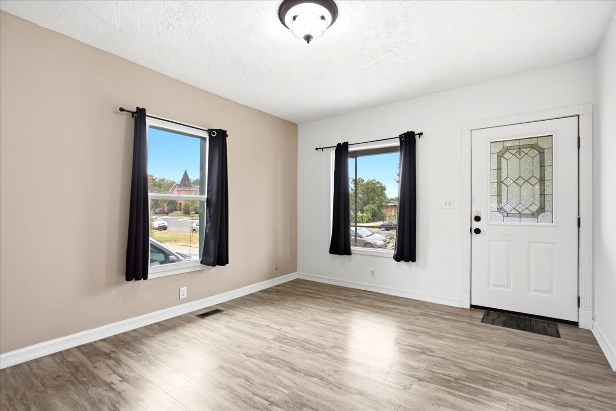 Spacious room featuring wood-finish flooring, two windows with black curtain rods, and a ceiling-mounted light fixture