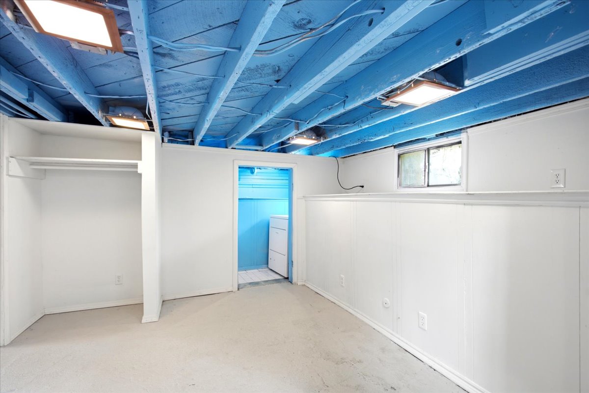 Lower-level room featuring an open ceiling with painted blue joists, white paneled walls with a chair rail, built-in closet with shelving and hanging rod, and recessed lighting