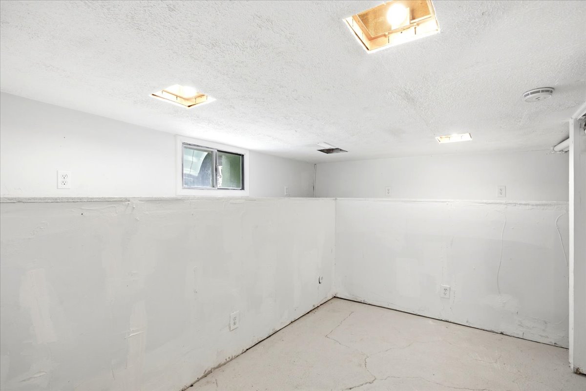 Unfinished room featuring white painted walls, a window for natural light, and overhead lighting fixtures