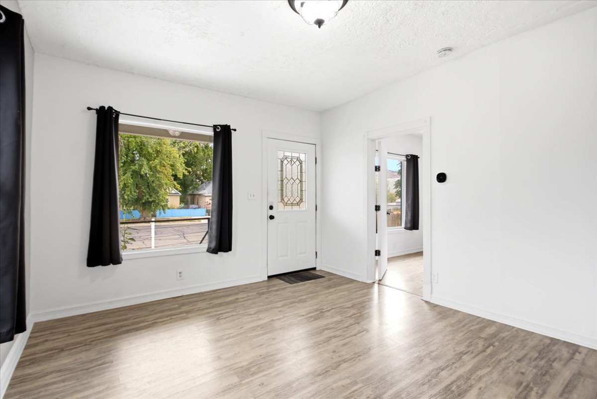 Bright interior space featuring light wood-finish flooring, white walls, and a front door with decorative glass