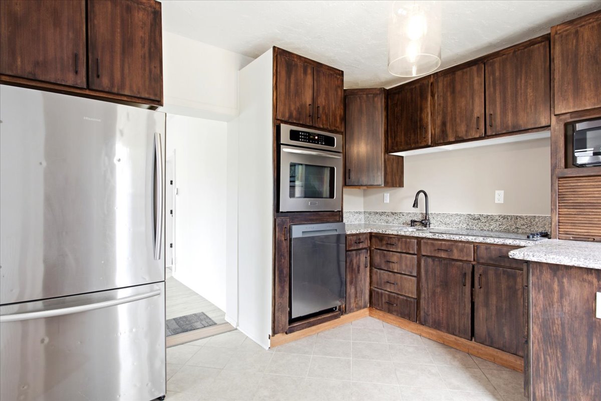 Kitchen featuring wood-finish cabinetry, granite countertops with matching backsplash, and stainless steel appliances including a built-in microwave and dishwasher