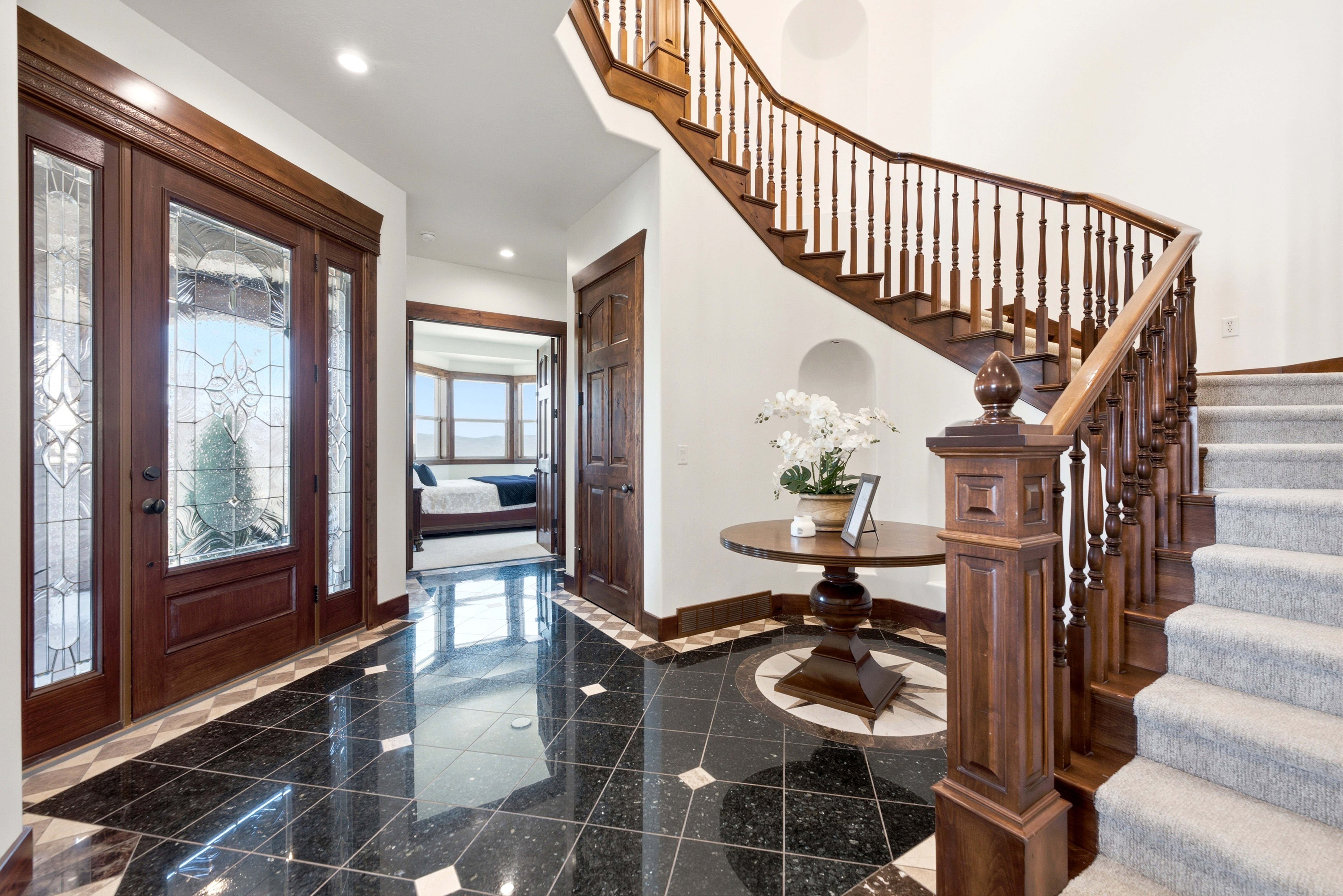 Grand entry featuring a dark wood staircase with ornate balusters, black tile flooring, and a decorative tile inlay
