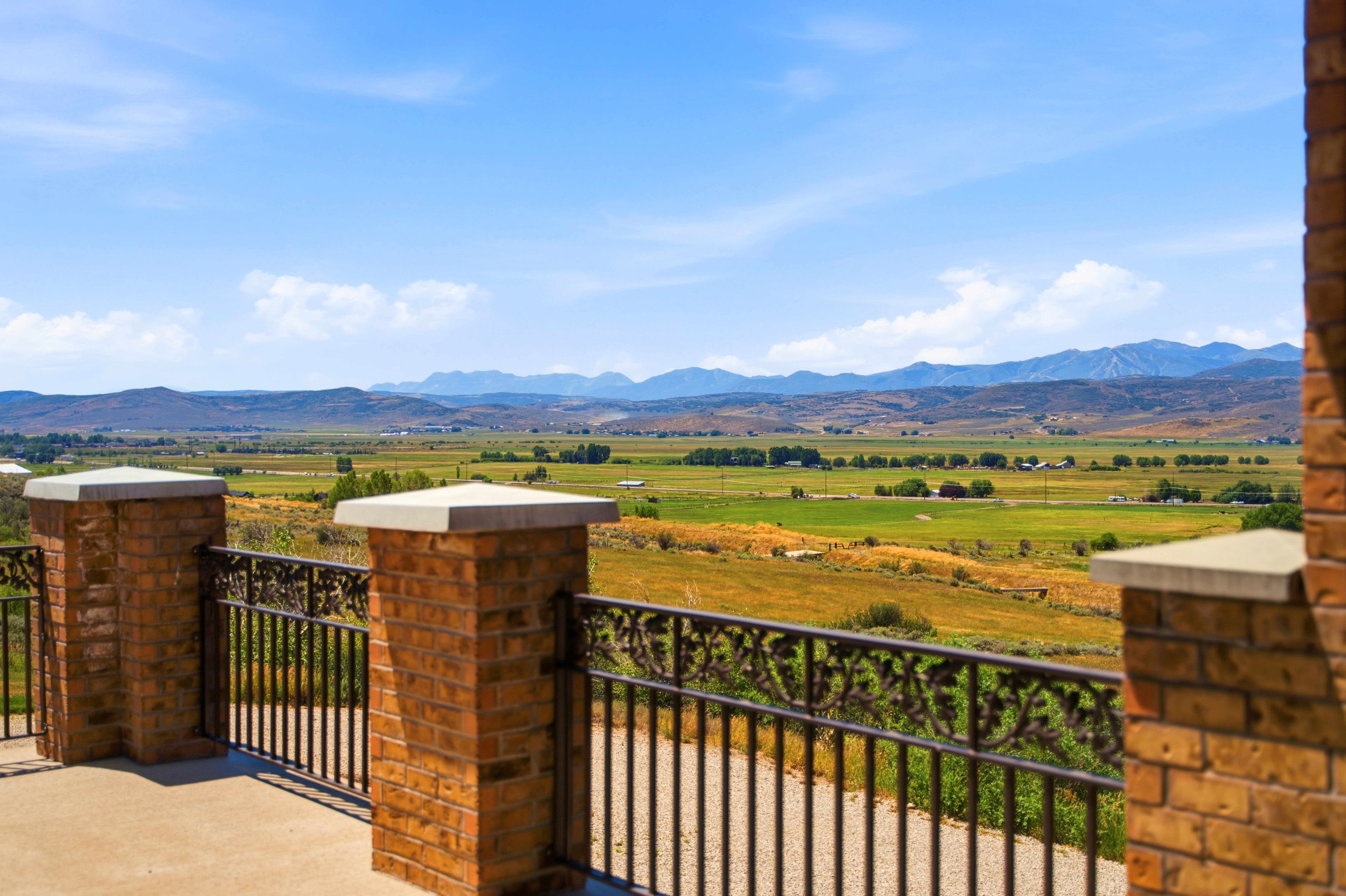 Exterior balcony featuring brick pillars with capstones and decorative metal railing, overlooking expansive green fields and distant mountains
