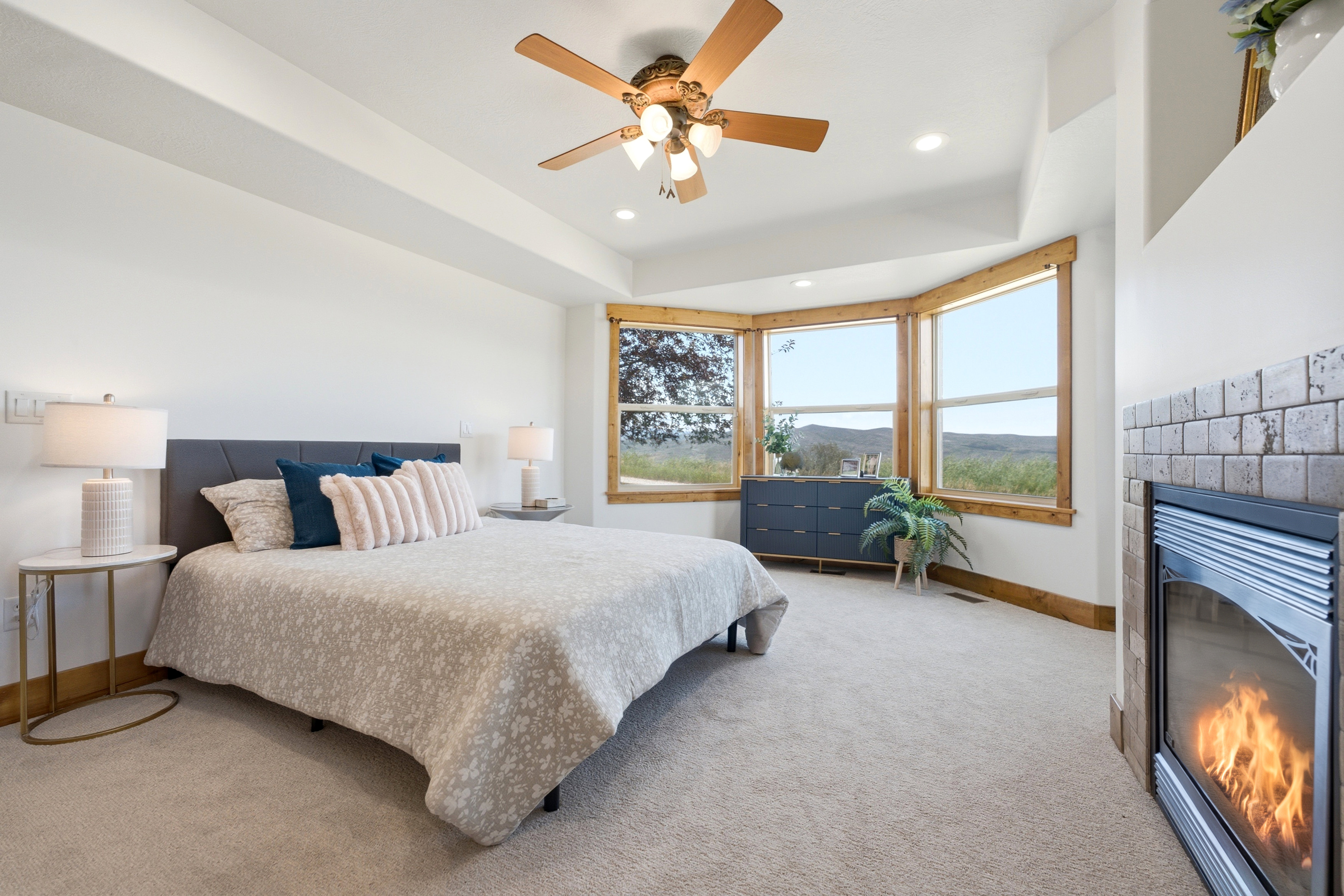 Bedroom featuring a multi-pane bay window with natural wood trim, a ceiling fan with integrated lighting, recessed lighting, and a built-in fireplace with a tiled surround