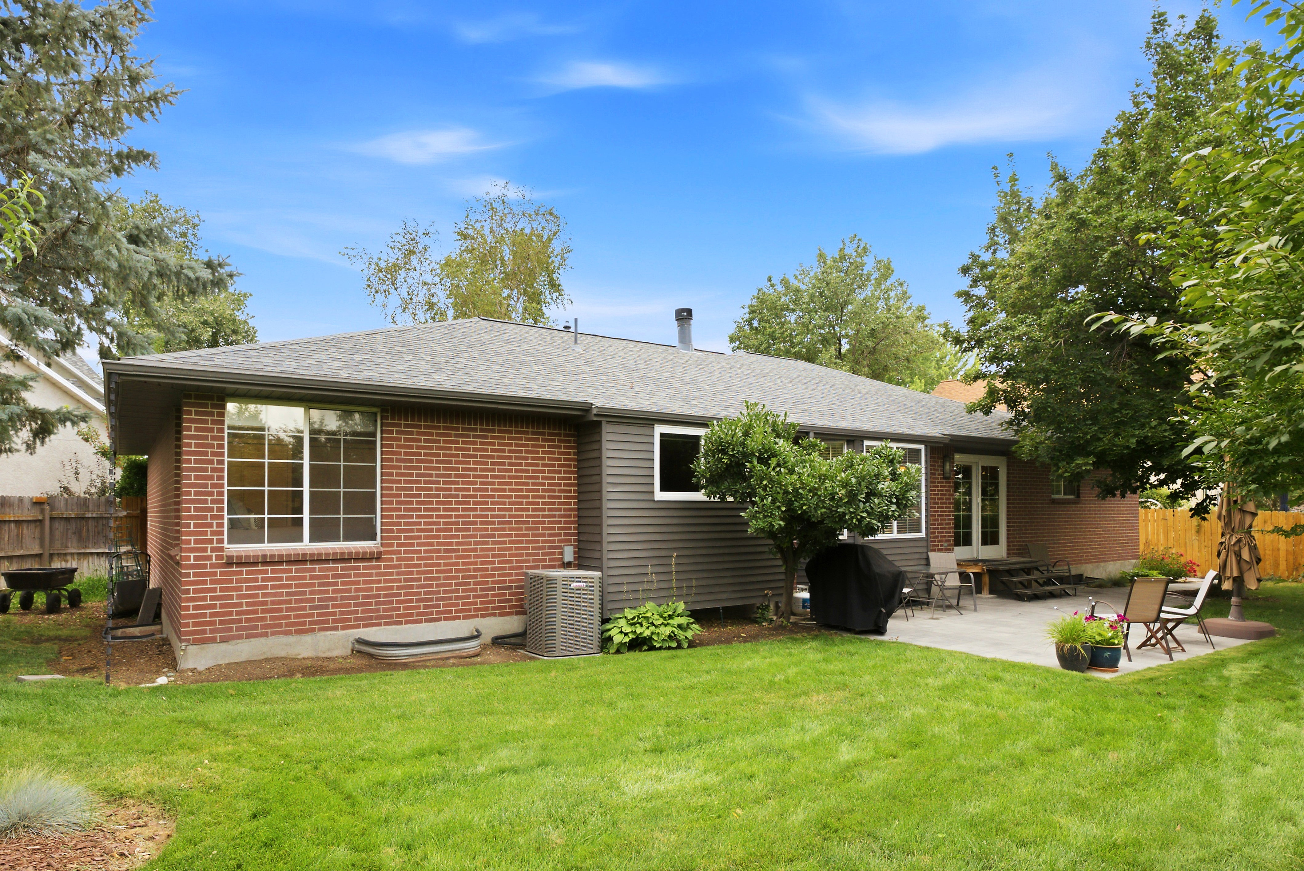 Expansive backyard featuring a large paver patio, brick exterior wall, mature trees, manicured lawn, and fully fenced yard. Perfect for entertaining!