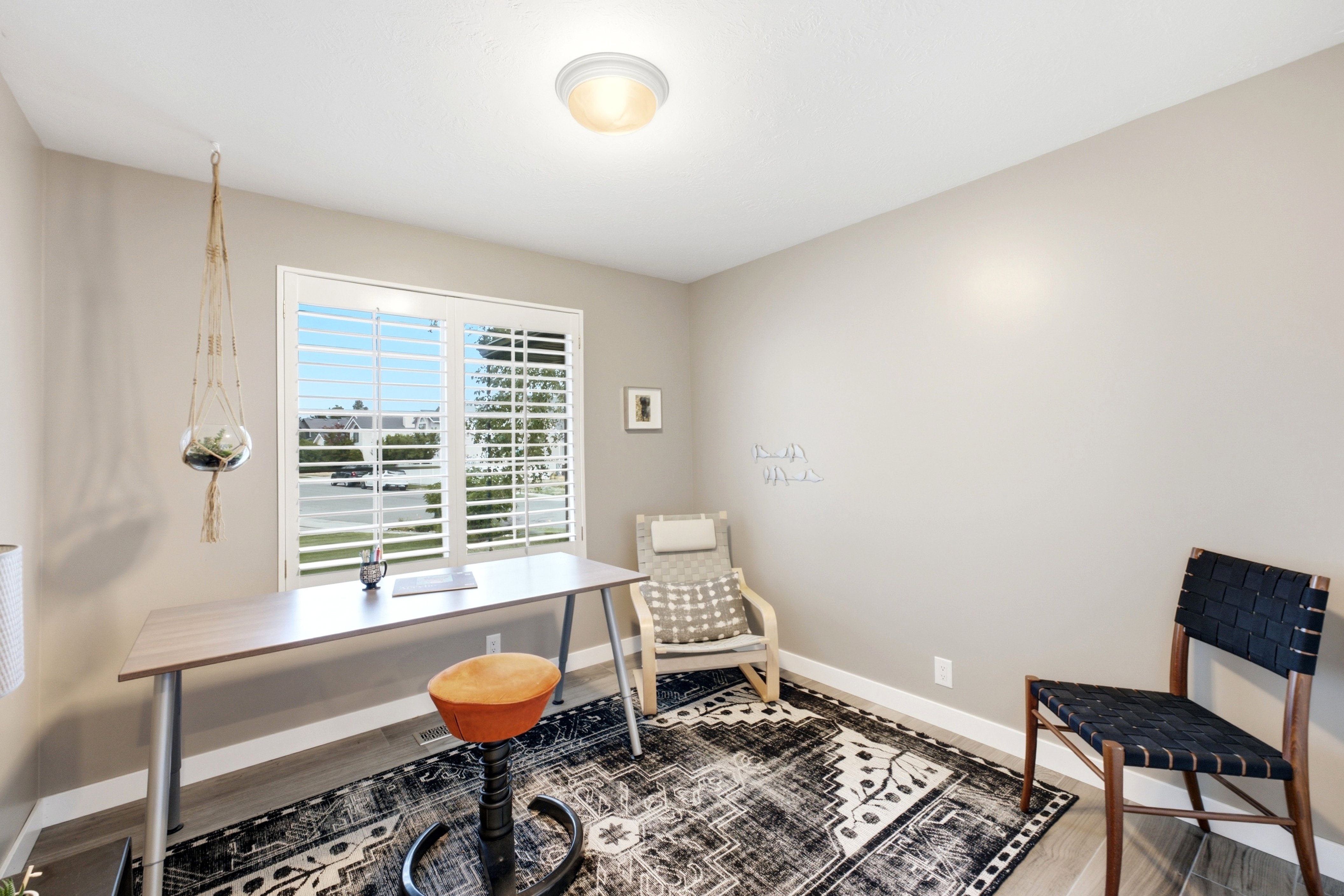 Bright room with light wood-finish flooring, neutral wall paint, and a large window featuring white plantation shutters