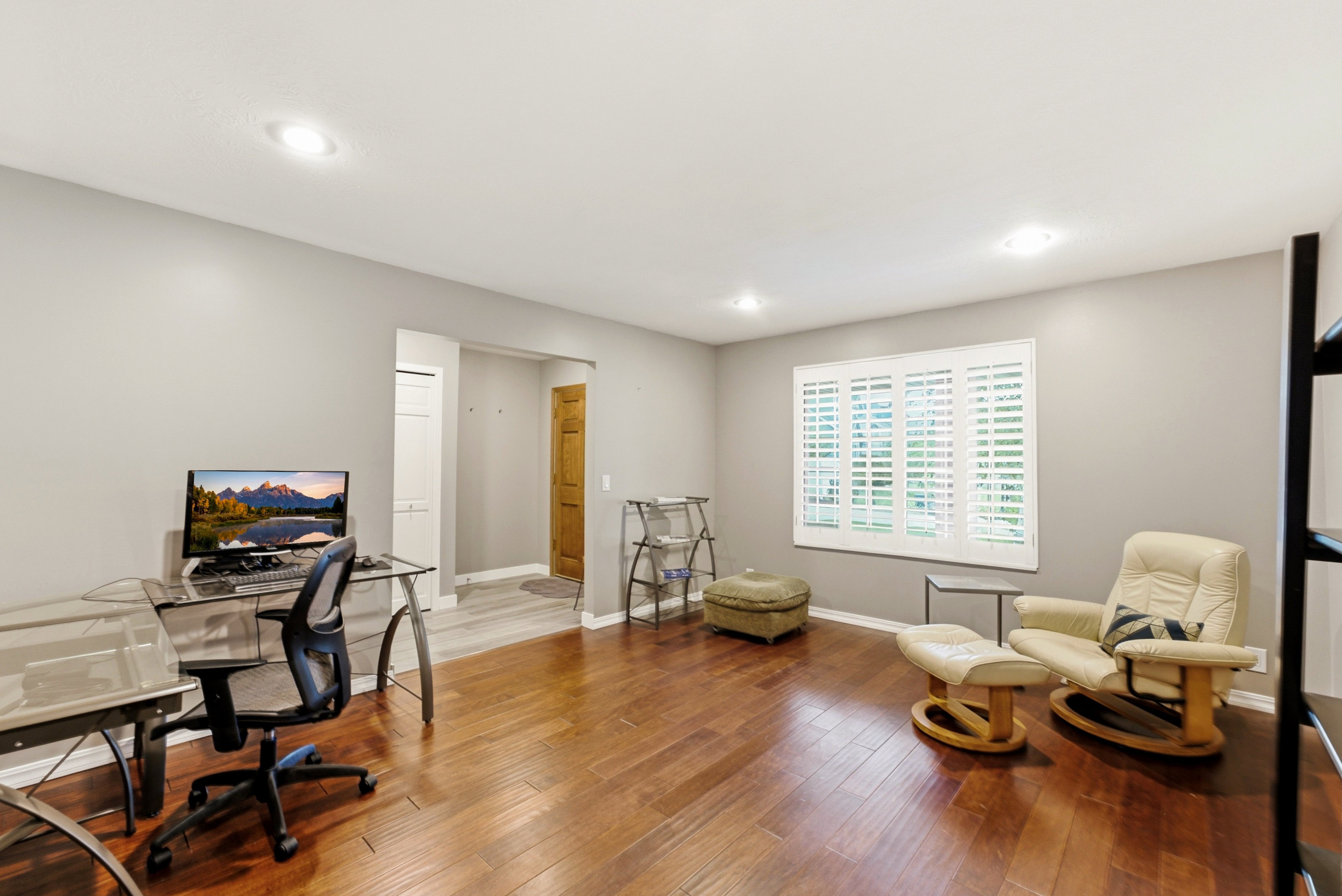 Spacious room at the entrance of home. Could be den, office or front room. Featuring rich wood-finish flooring, recessed lighting, and a window with white plantation shutters.