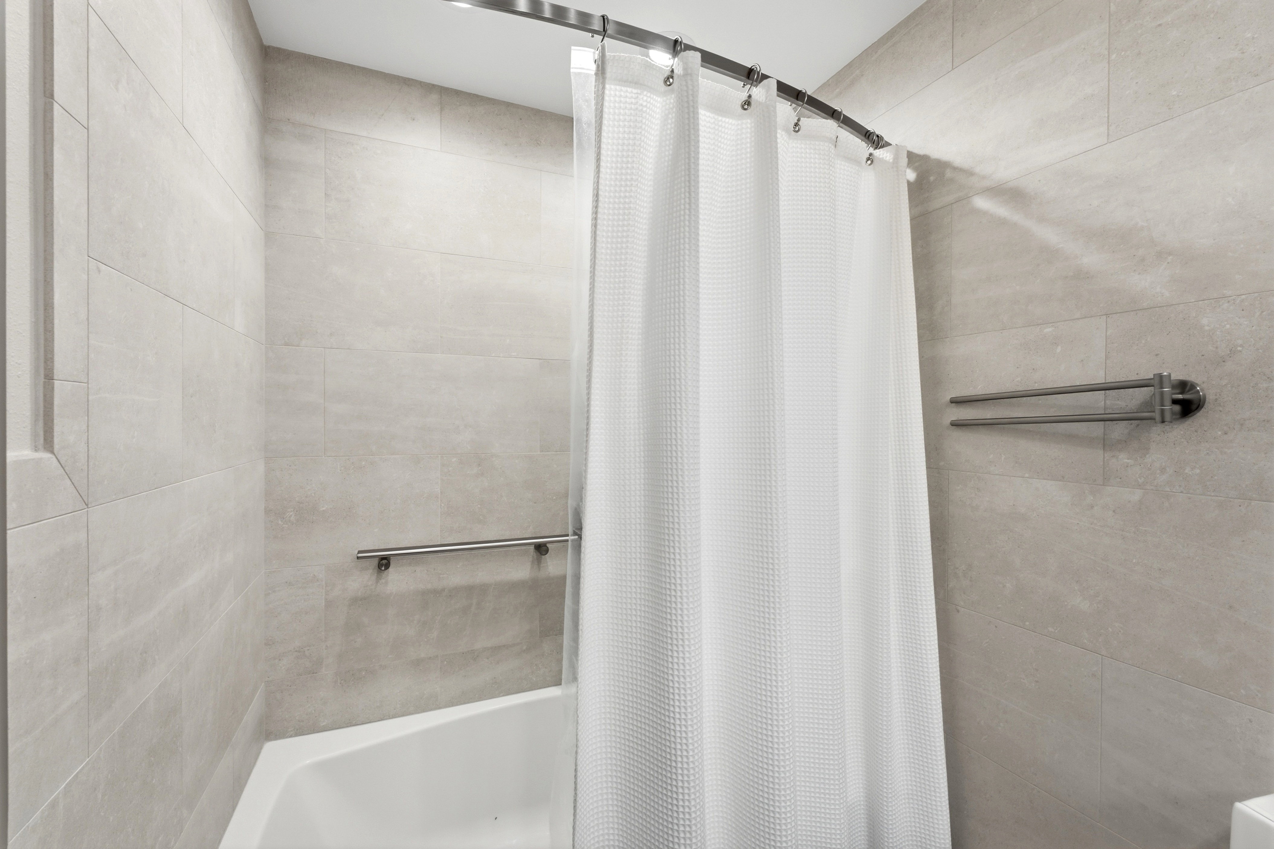 Bathtub with light-toned wall tiling, a curved shower rod, and a wall-mounted towel bar
