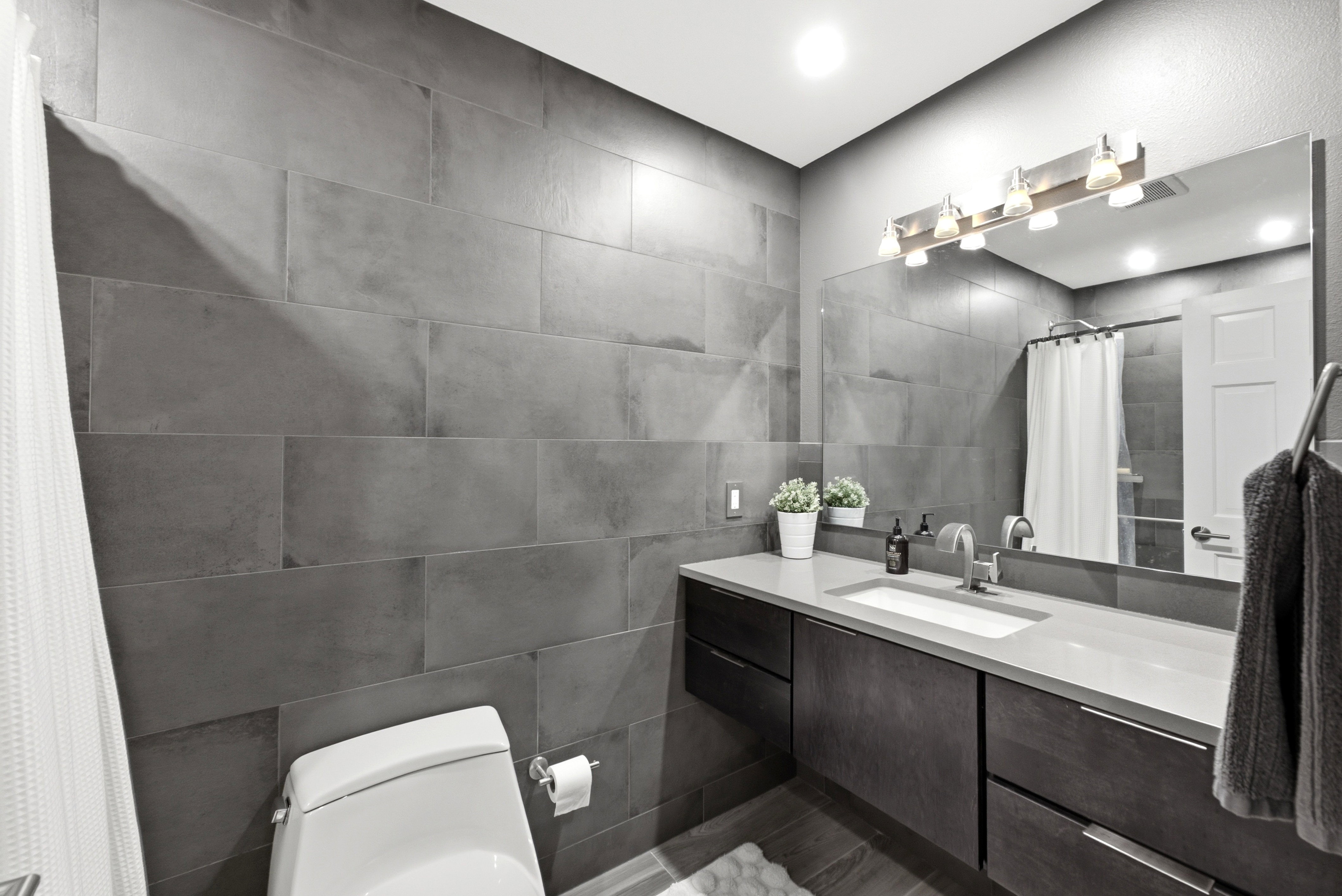 Full tile modern bathroom featuring a vanity with a white rectangular undermount sink, a light-toned countertop, and dark wood-finish cabinetry
