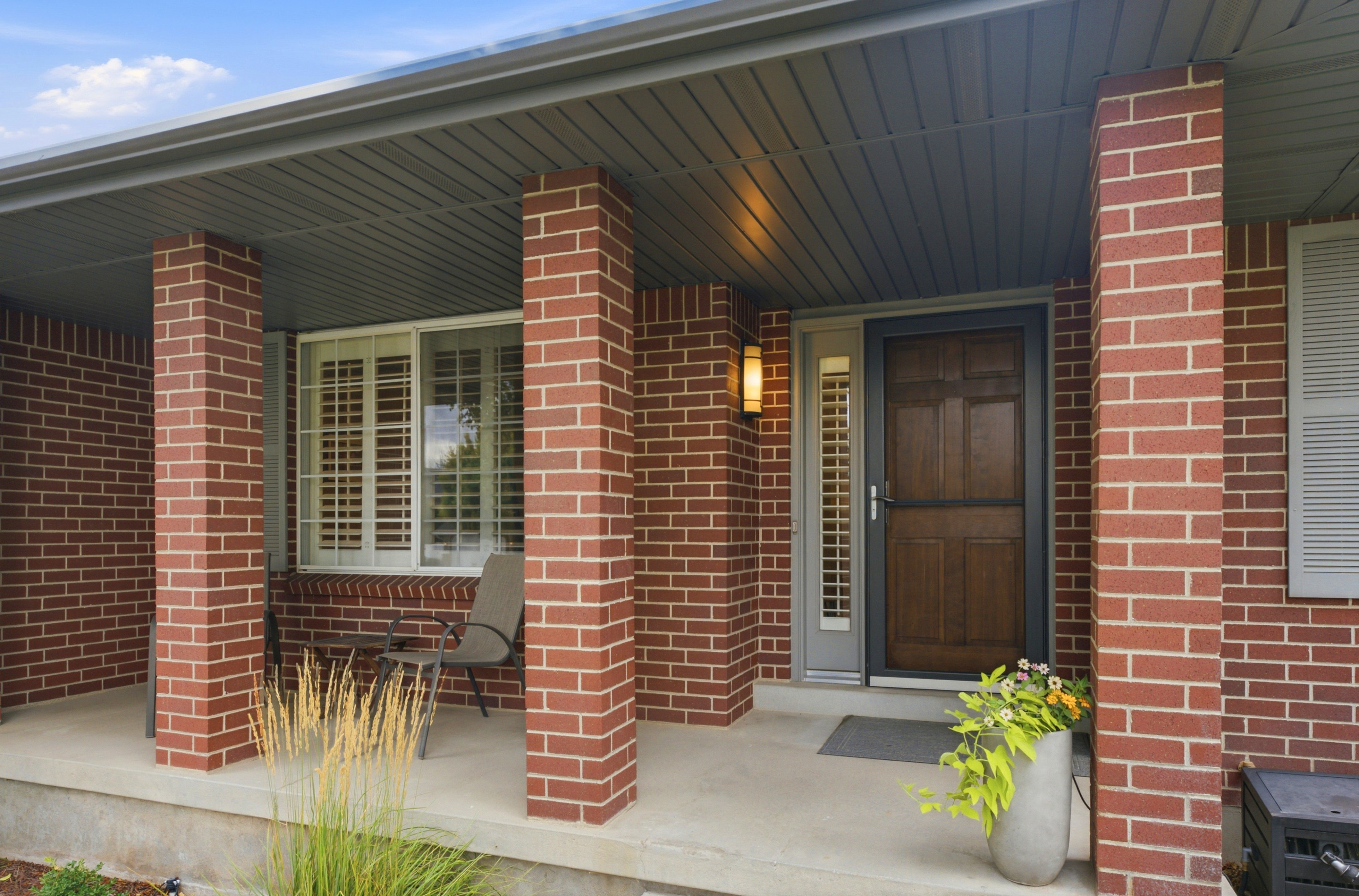 Brick facade with a covered porch featuring a dark wood-finish entry door, a sidelight window, and a wall-mounted exterior light fixture