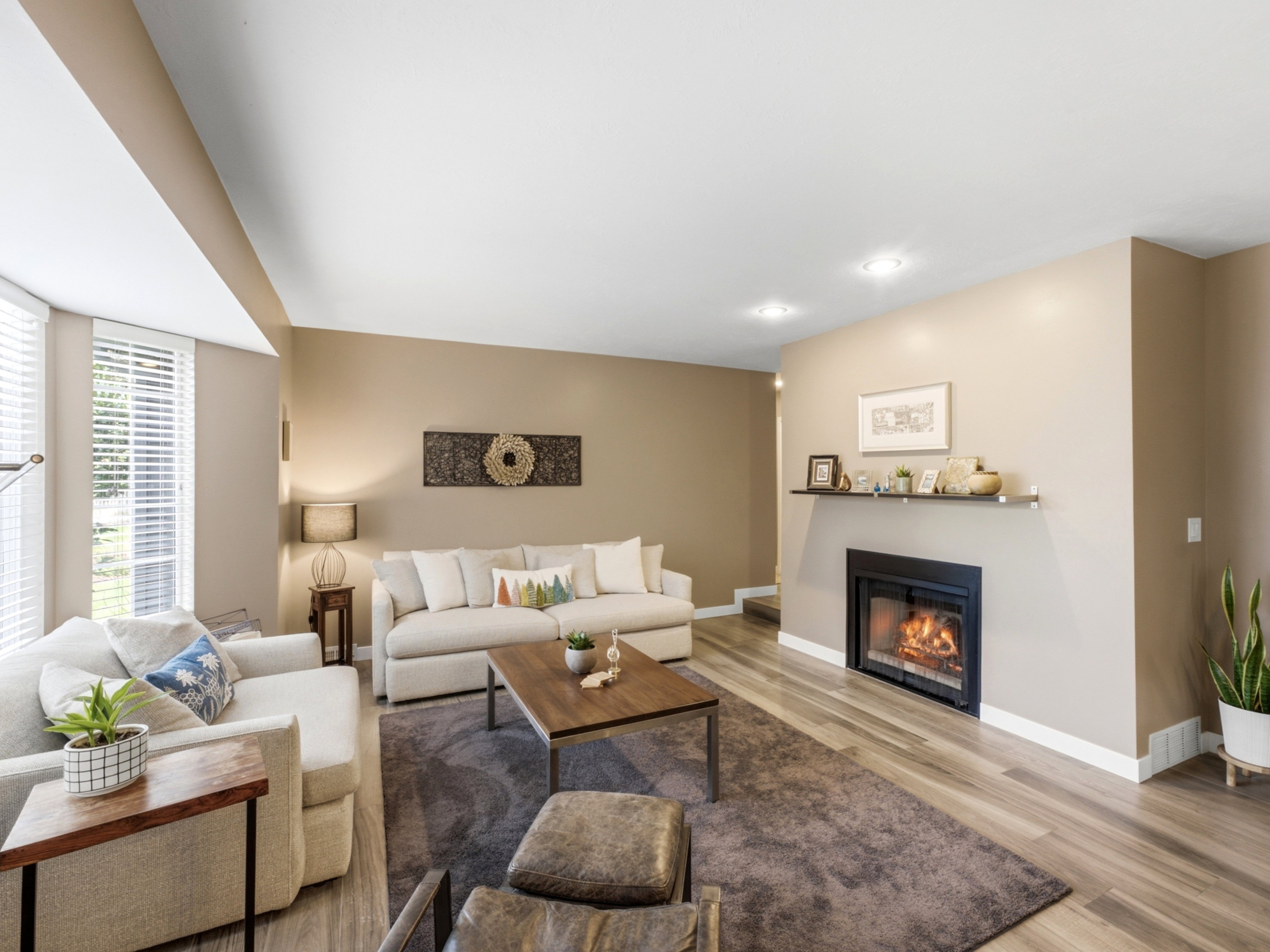 Main level family room  featuring wood-finish flooring, a built-in gas fireplace with a floating mantel, recessed lighting, and multiple windows with blinds.