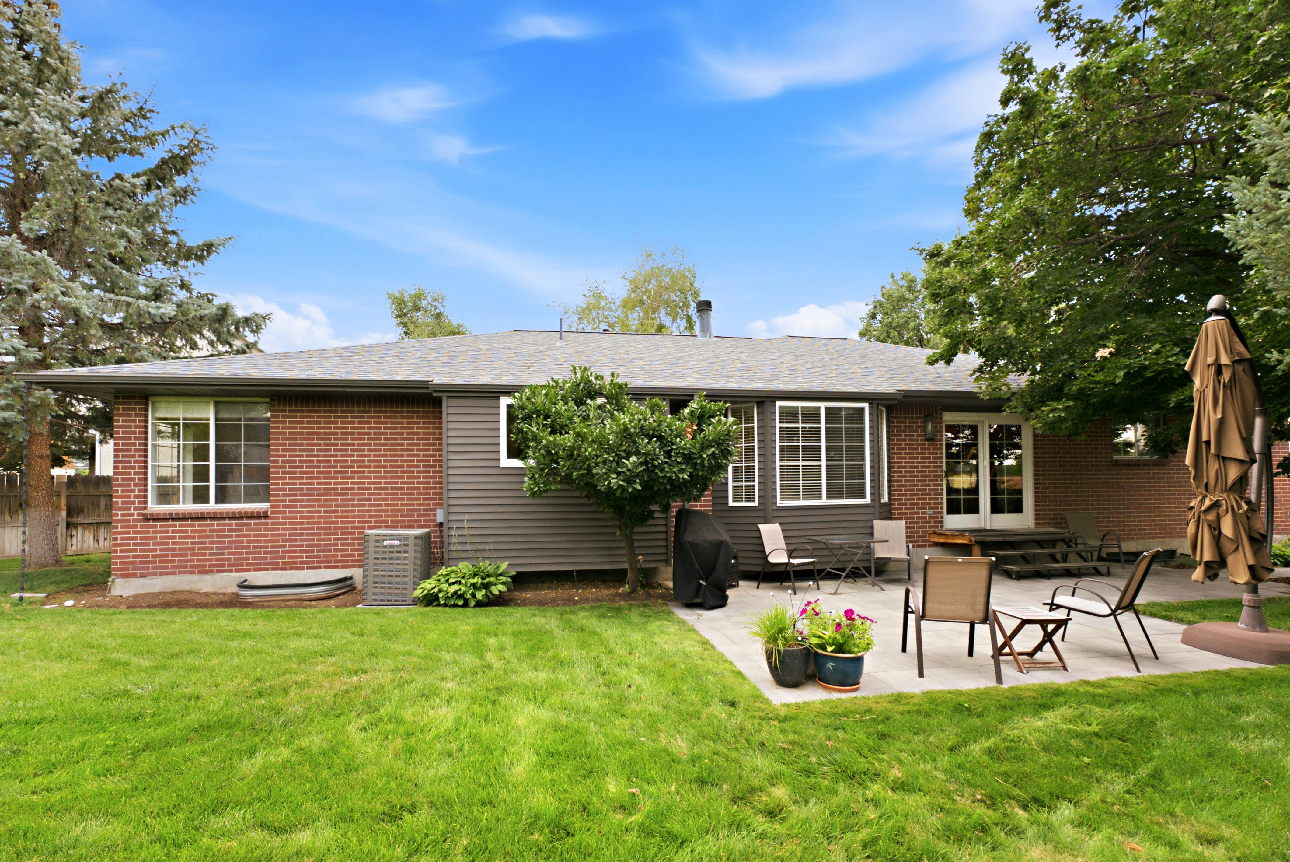 Expansive backyard featuring a large paver patio, brick exterior wall, mature trees, manicured lawn, and fully fenced yard. Perfect for entertaining!