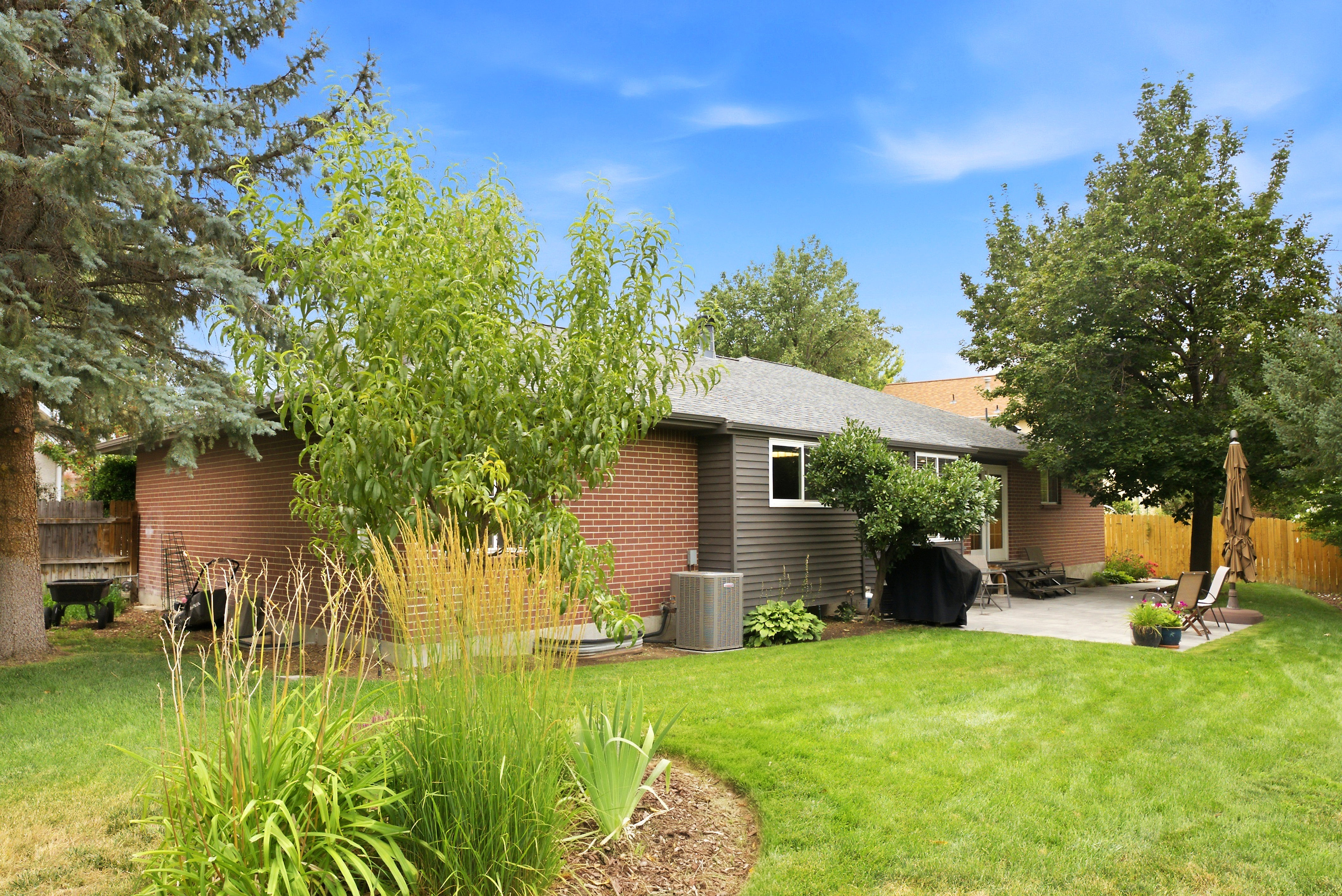 Expansive backyard featuring a large paver patio, brick exterior wall, mature trees, manicured lawn, and fully fenced yard. Perfect for entertaining!