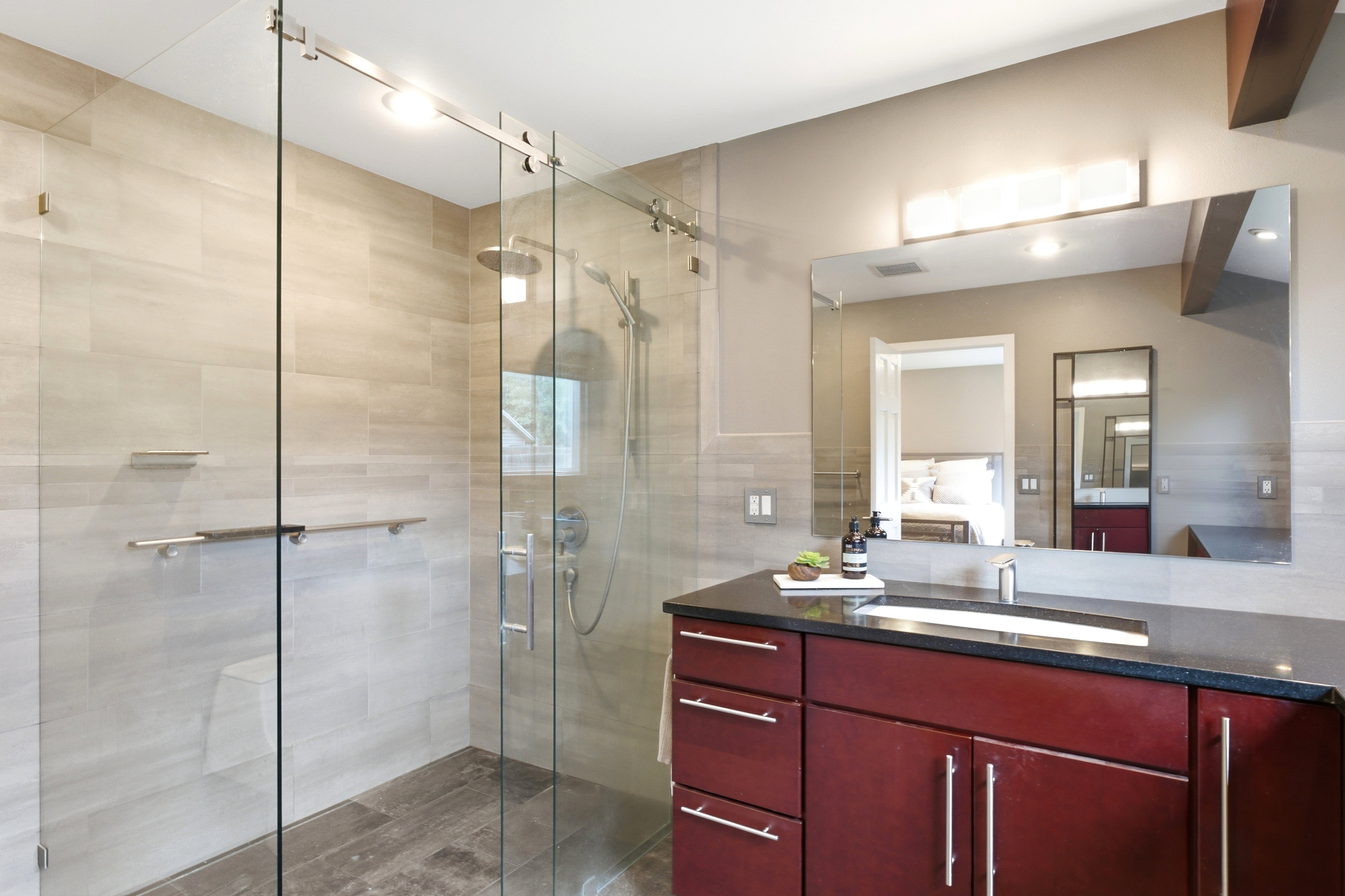 Spacious master bathroom featuring a glass-enclosed shower with a rain showerhead, light-toned wall tile, a dark wood-finish vanity with a gorgeous countertop. Zero step shower!