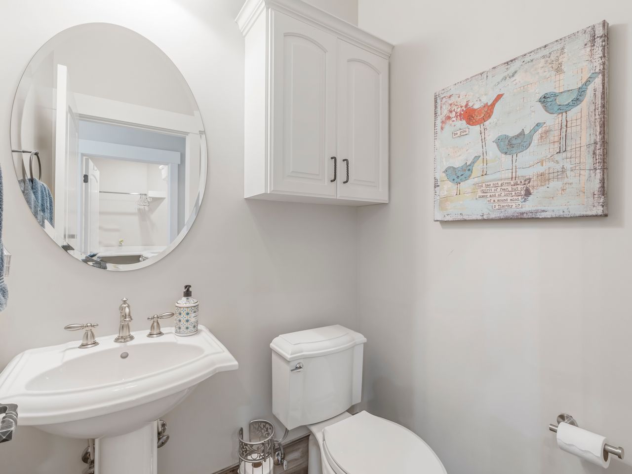 White pedestal sink with brushed nickel faucet, oval mirror, and wall-mounted storage cabinet