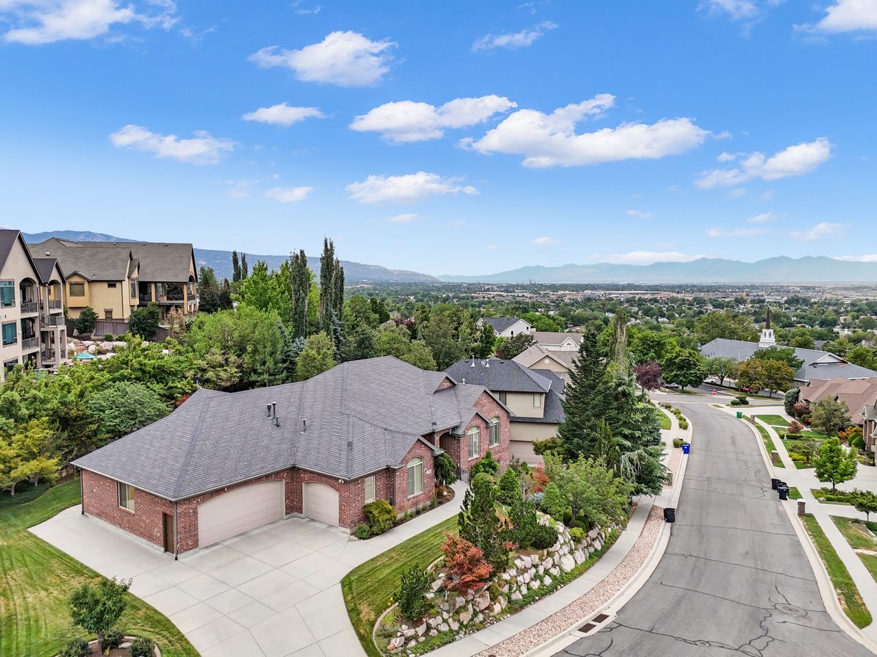 Brick exterior residence featuring a multi-car garage, mature landscaping, and a sloped, manicured lawn