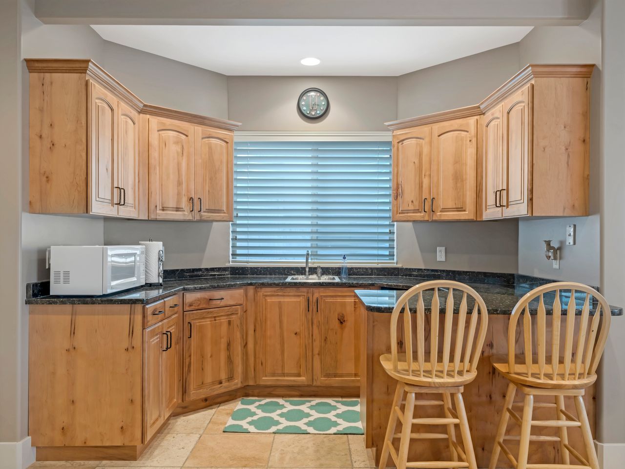 Built-in bar area featuring wood cabinetry, dark stone countertops, an undermount sink, and tiled flooring