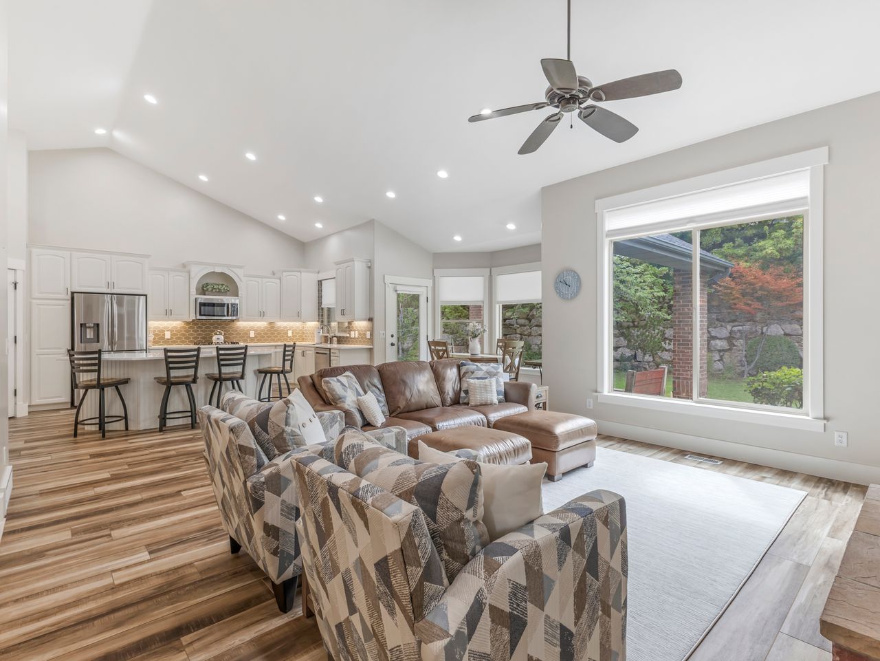 Open concept living space featuring vaulted ceilings, recessed lighting, wood-finish flooring, a ceiling fan, and large windows