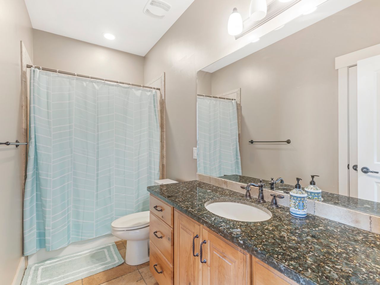 Bathroom vanity featuring a dark granite countertop, undermount sink, and wood-finish cabinetry with dark hardware