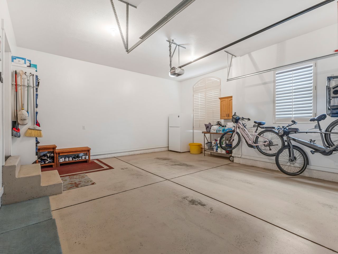 Spacious garage featuring a concrete floor, bright overhead lighting, and two windows with white plantation shutters