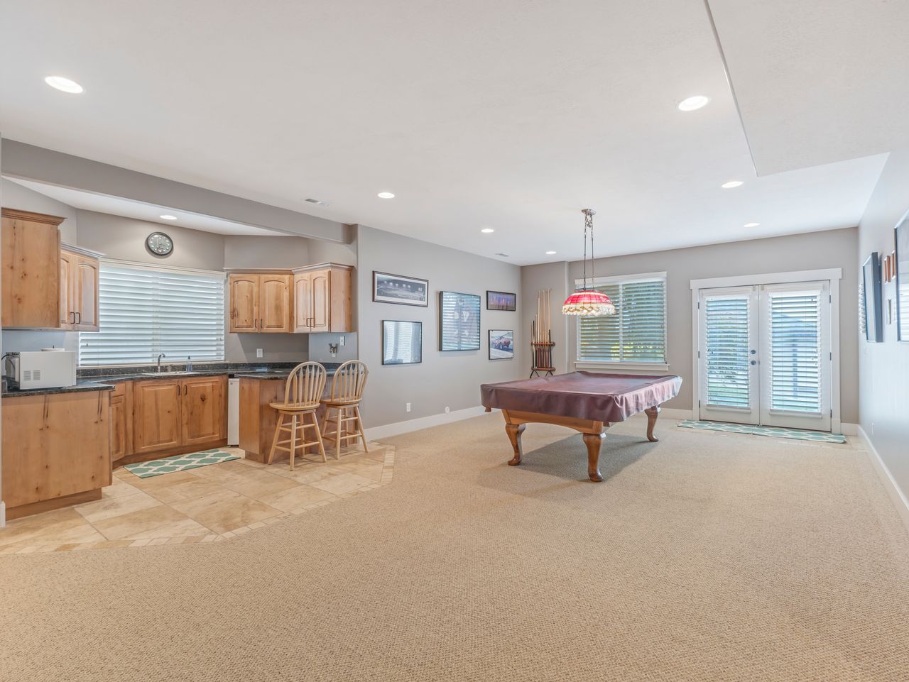 Spacious entertainment area featuring a wet bar with wood cabinetry and dark countertops, recessed lighting, double French doors, and carpet flooring