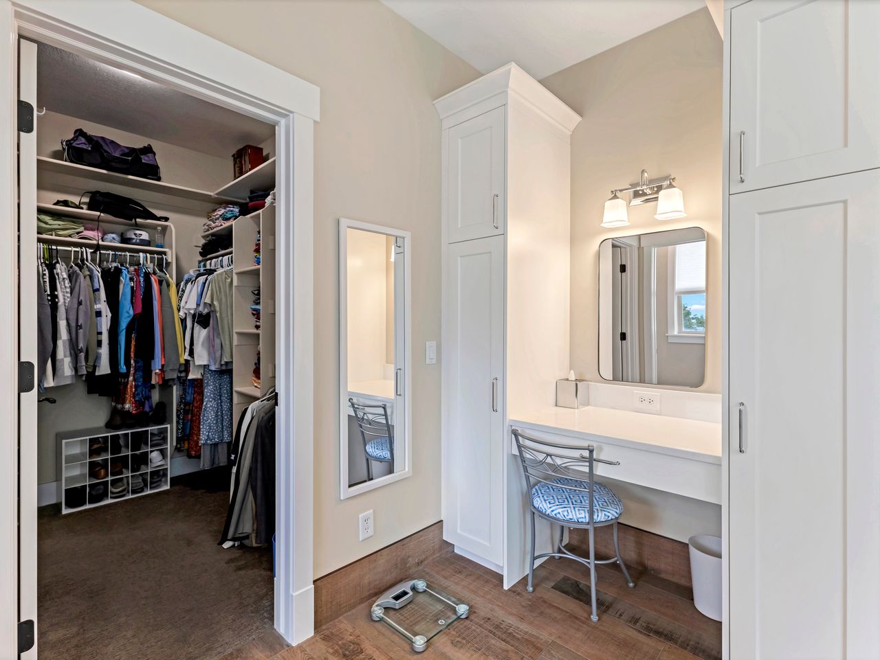Dressing area with wood-finish flooring, white built-in cabinetry, a vanity counter, and an illuminated wall mirror