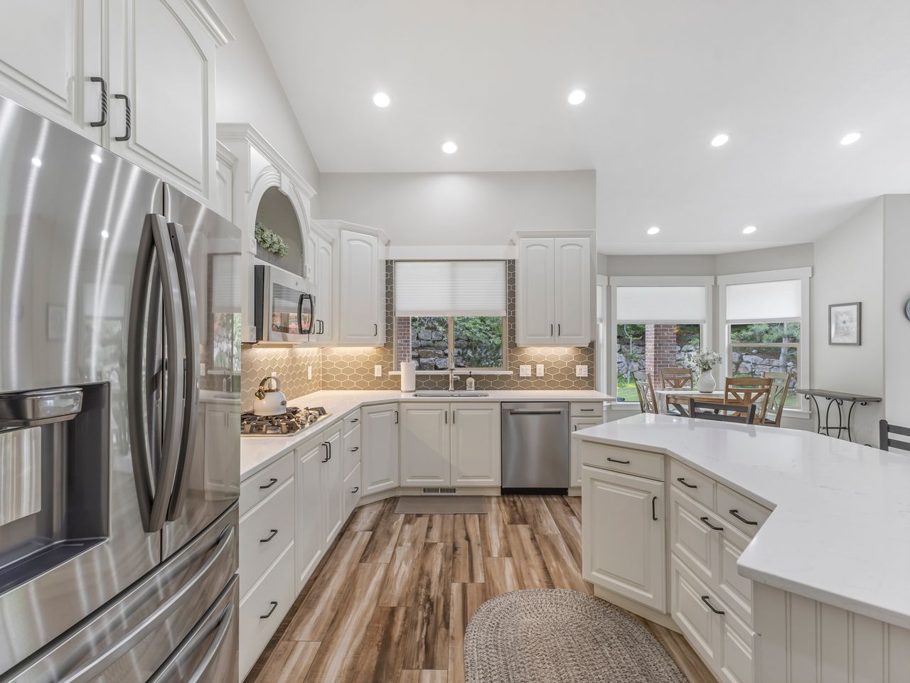 Kitchen featuring white cabinetry, stainless steel appliances, wood-finish flooring, light countertops, and a tile backsplash