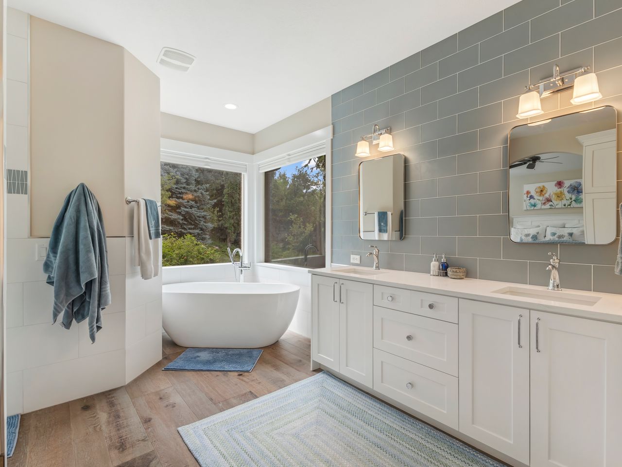 Bathroom featuring a freestanding soaking tub, wood-finish flooring, and a double vanity with white cabinetry and integrated sinks