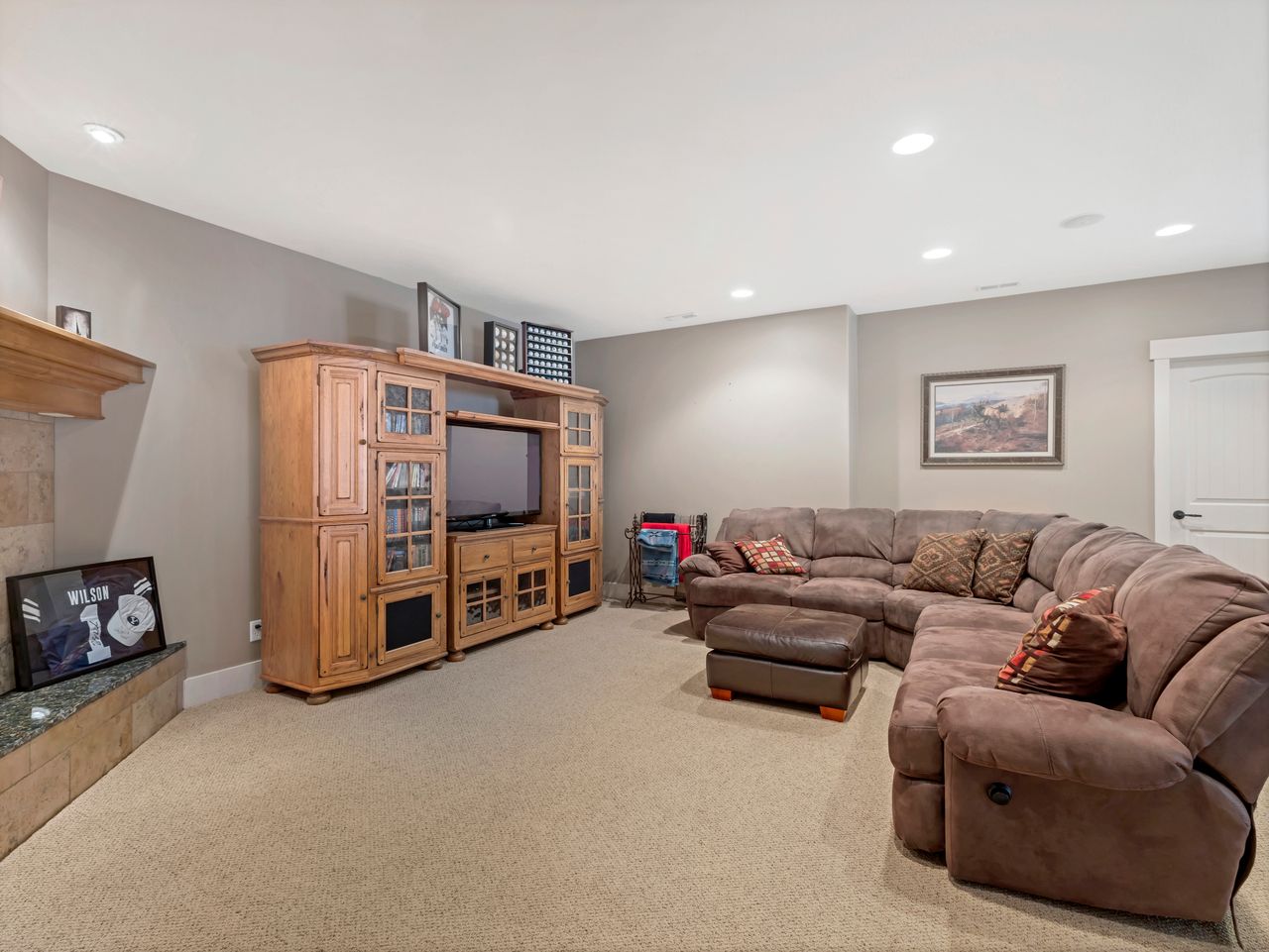Carpeted recreation room featuring recessed lighting, a fireplace with a stone hearth and wood mantle, and a white interior door