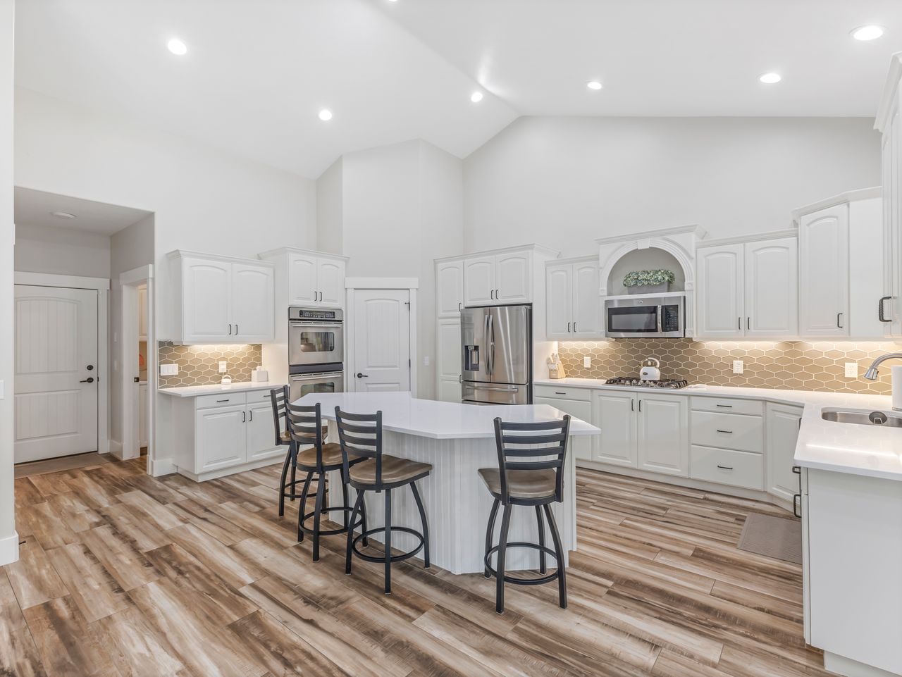 Spacious kitchen featuring vaulted ceilings, wood-finish flooring, white cabinetry, stainless steel appliances, and a central island with seating