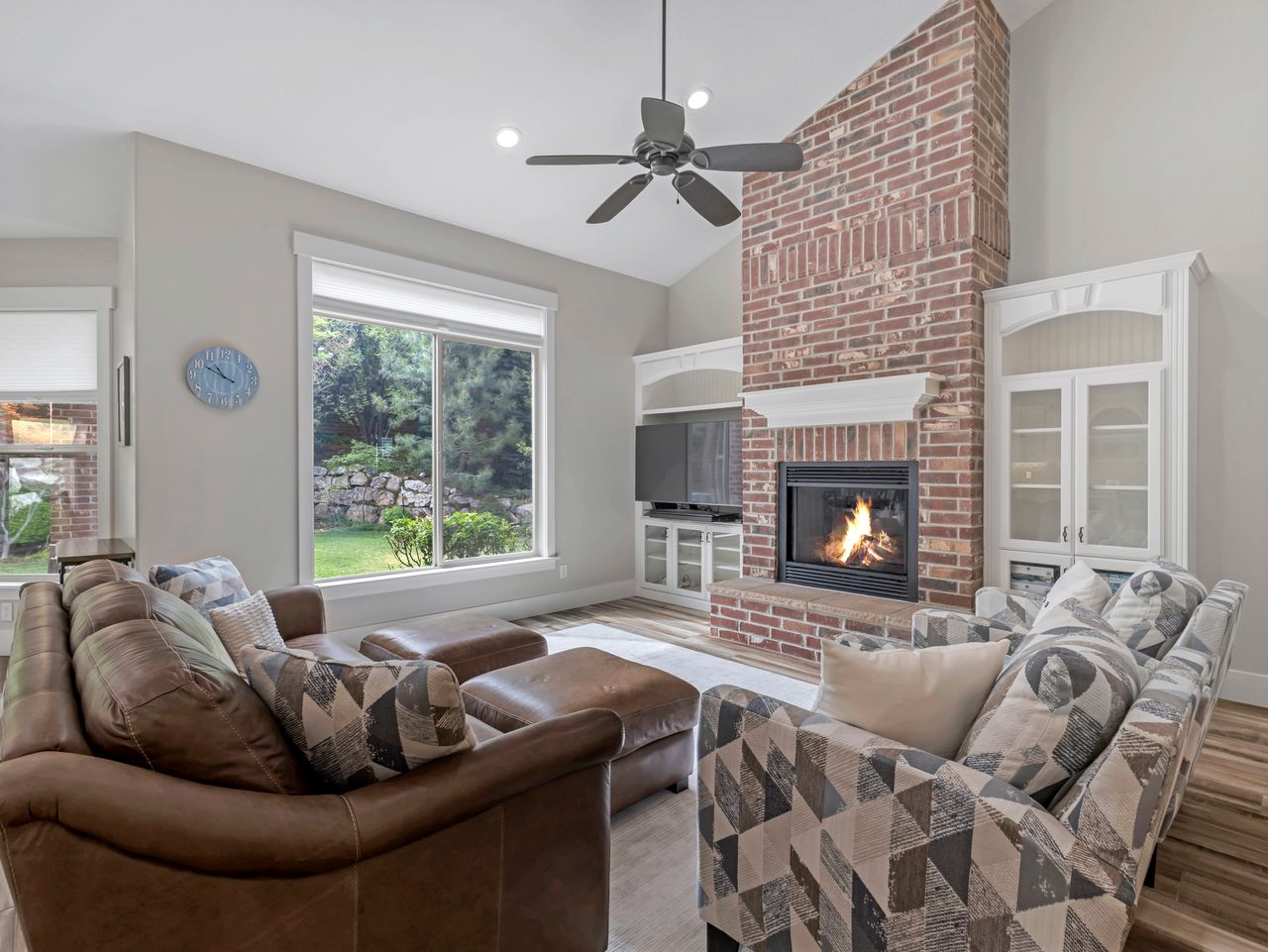 Living area featuring a floor-to-ceiling brick fireplace with a white mantel, vaulted ceilings, and built-in cabinetry with glass doors
