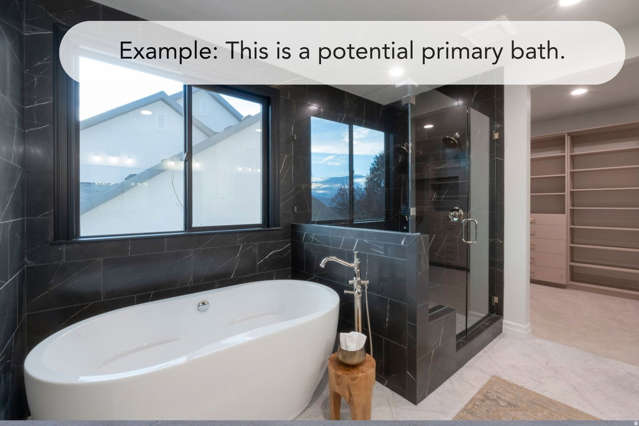 Freestanding soaking tub with floor-mounted faucet, surrounded by dark marbled tile walls and a large window