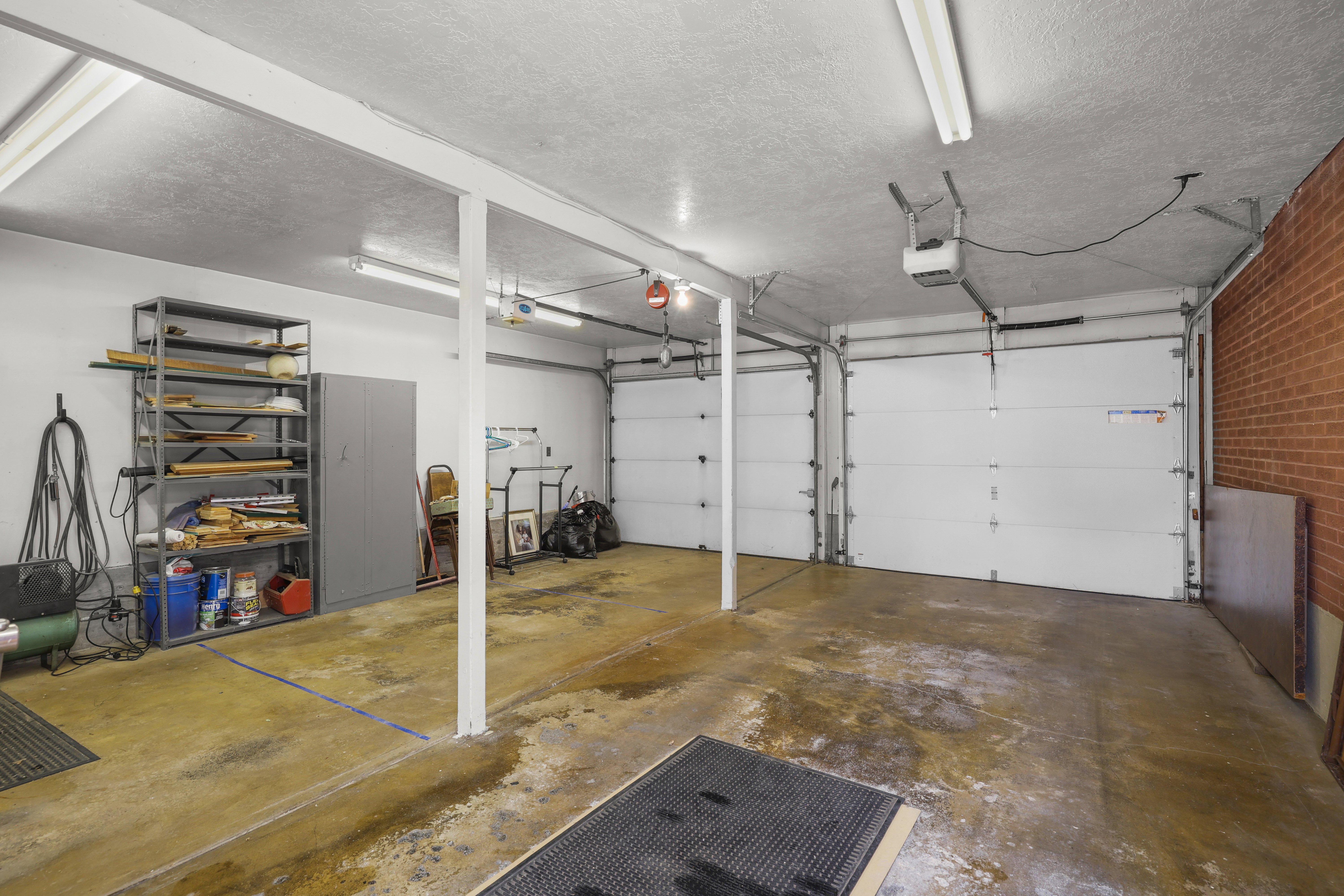 Spacious two-car garage featuring automatic openers, exposed brick accents, fluorescent lighting, and a concrete floor