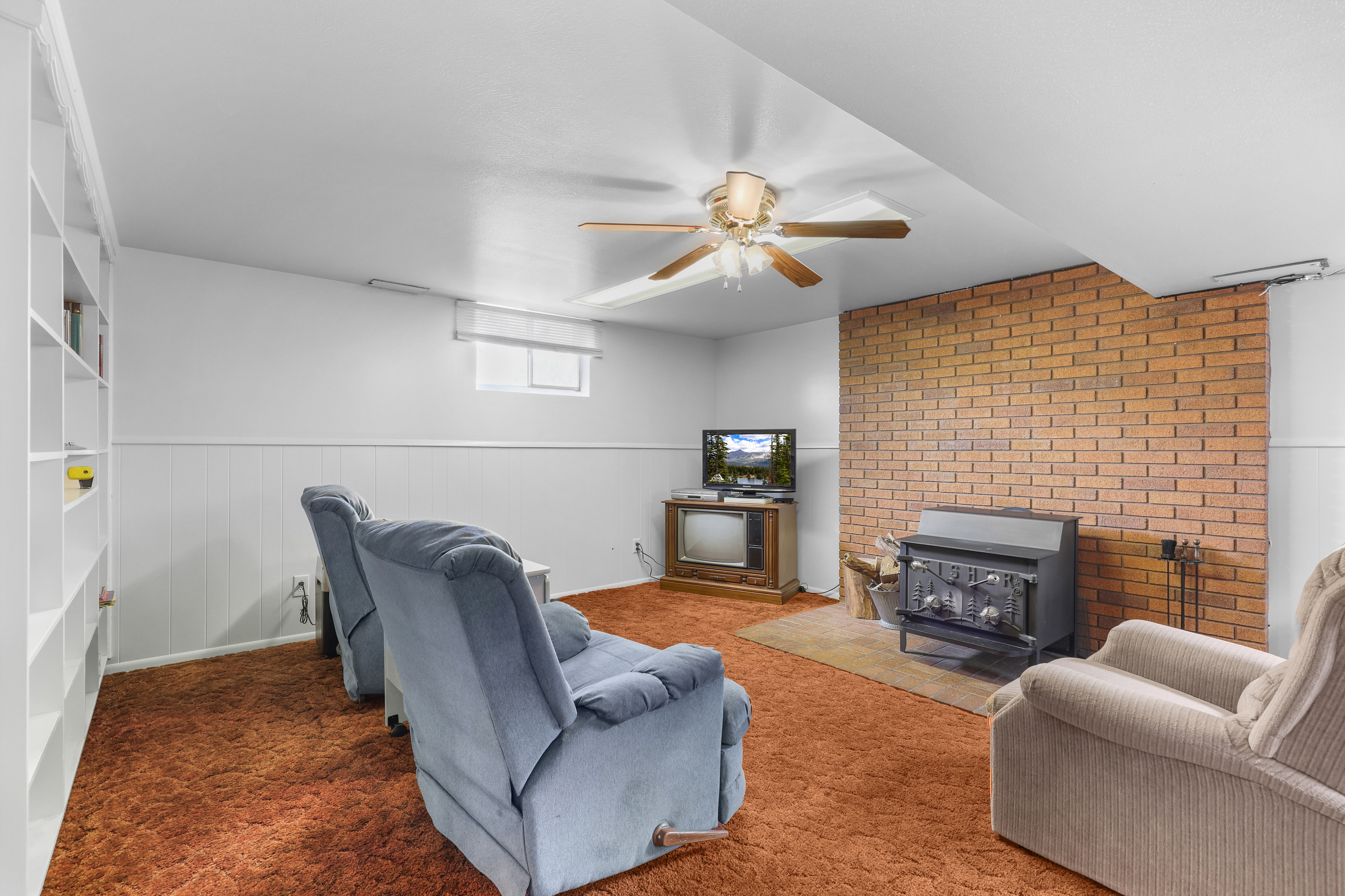 Living space featuring a brick accent wall, a cast-iron wood-burning stove, and built-in shelving