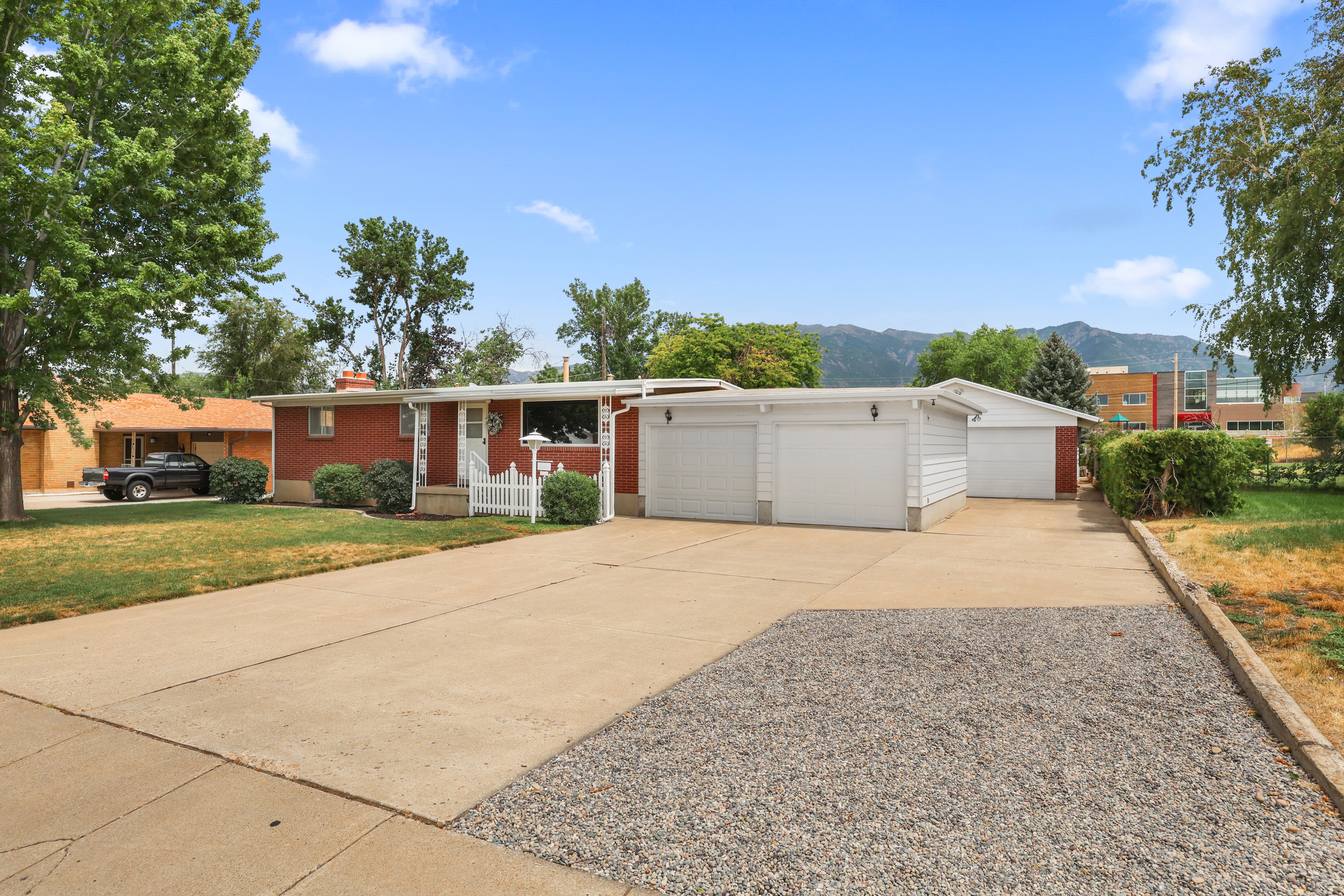 Brick-front residence featuring a spacious concrete driveway, multiple garage bays, and mature landscaping