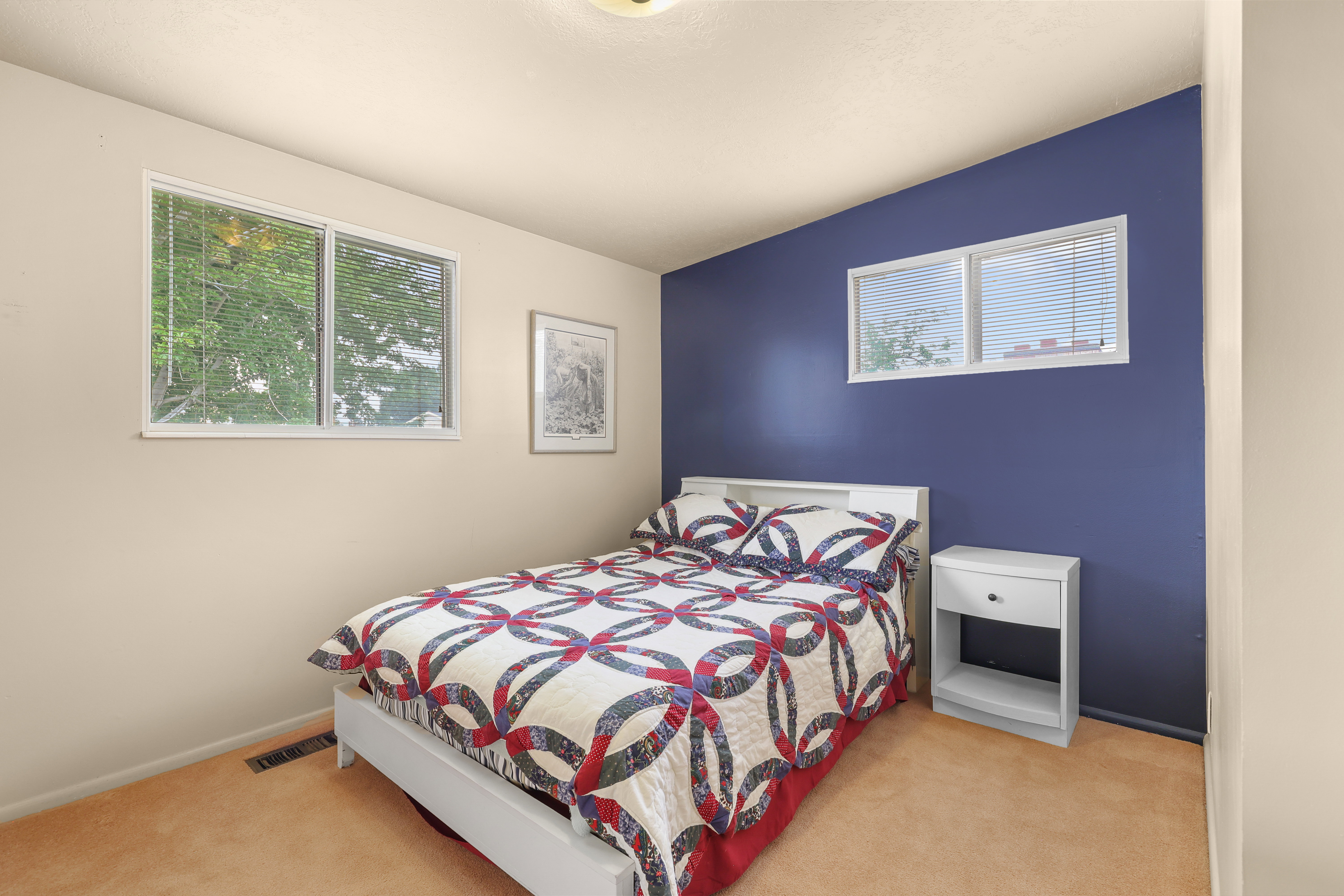 Bedroom featuring a prominent accent wall, two windows with white blinds, and light-colored carpeting