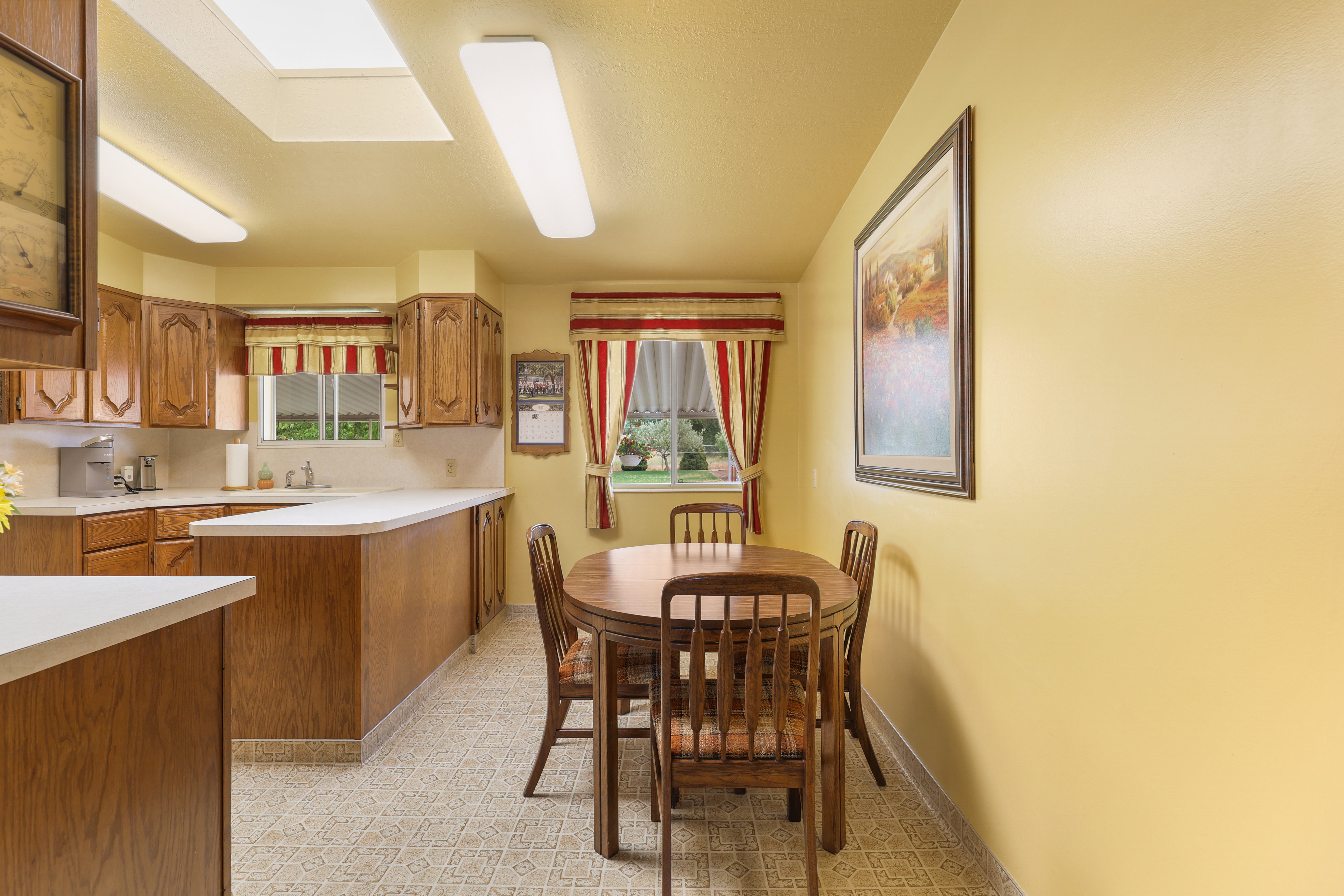 Kitchen and dining area featuring wood cabinetry, white countertops, a double basin sink, and a skylight