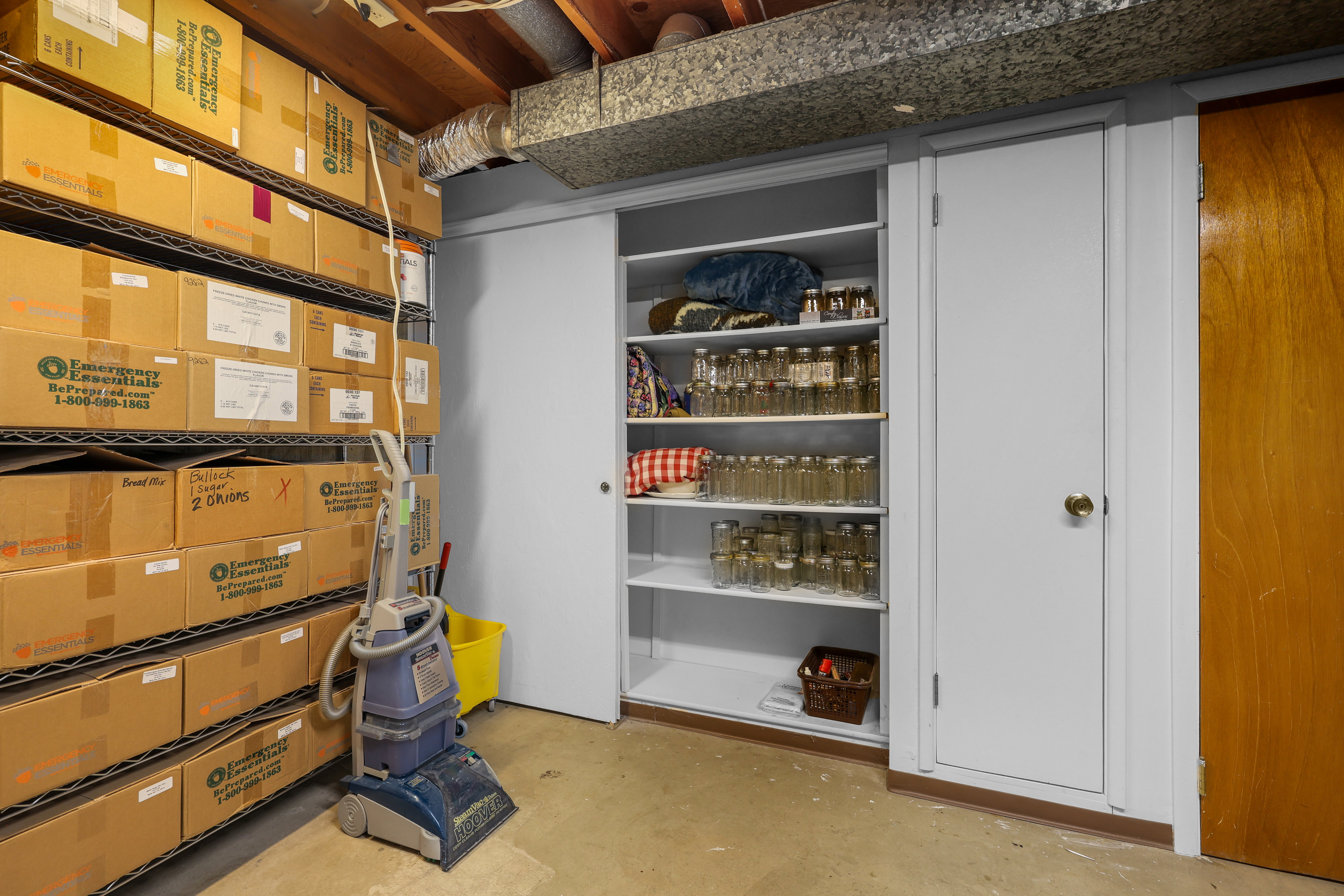 Basement storage area featuring built-in shelving, a wood-finish door, and exposed ceiling joists