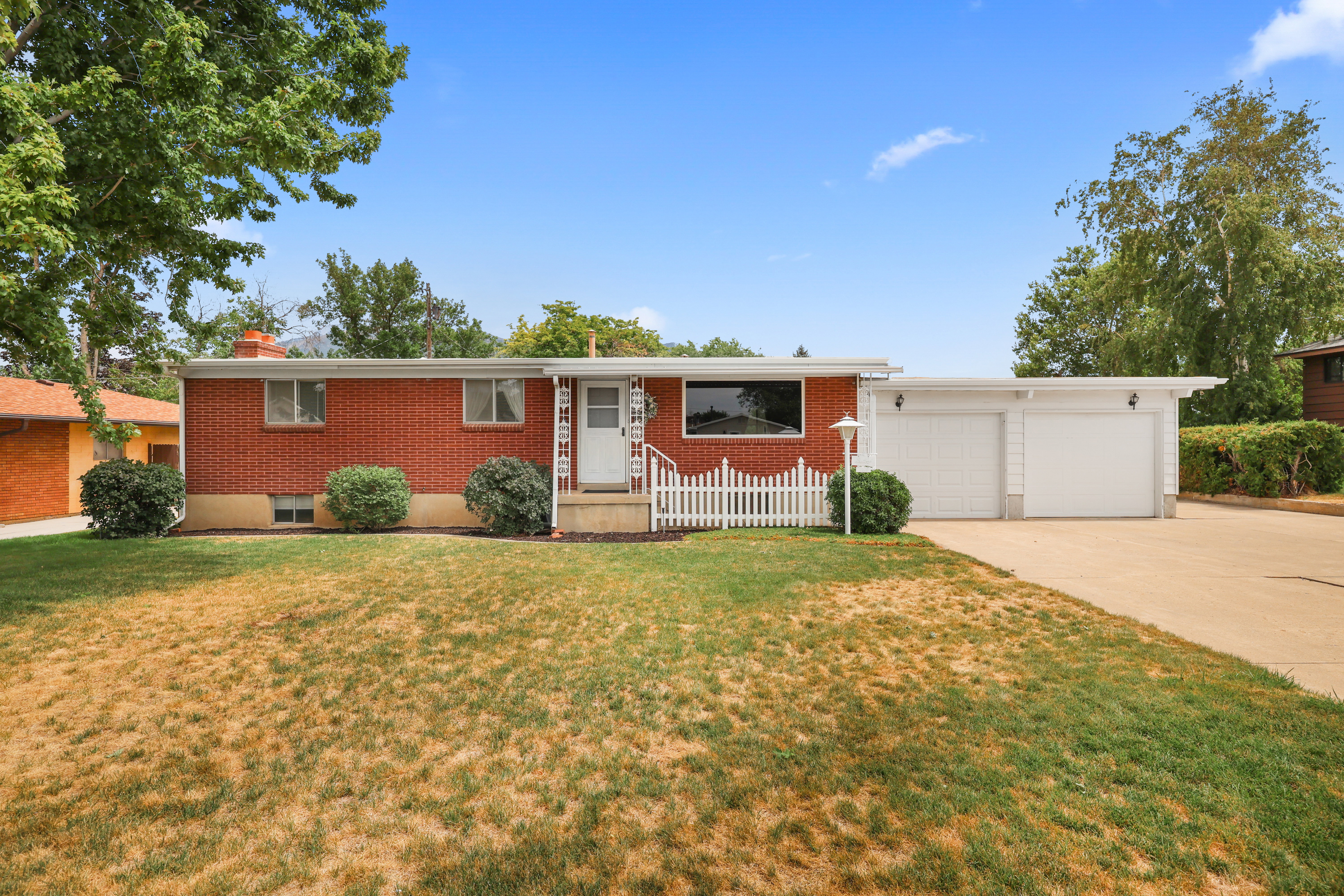 Brick exterior featuring a two-car garage, white picket fence, and mature landscaping