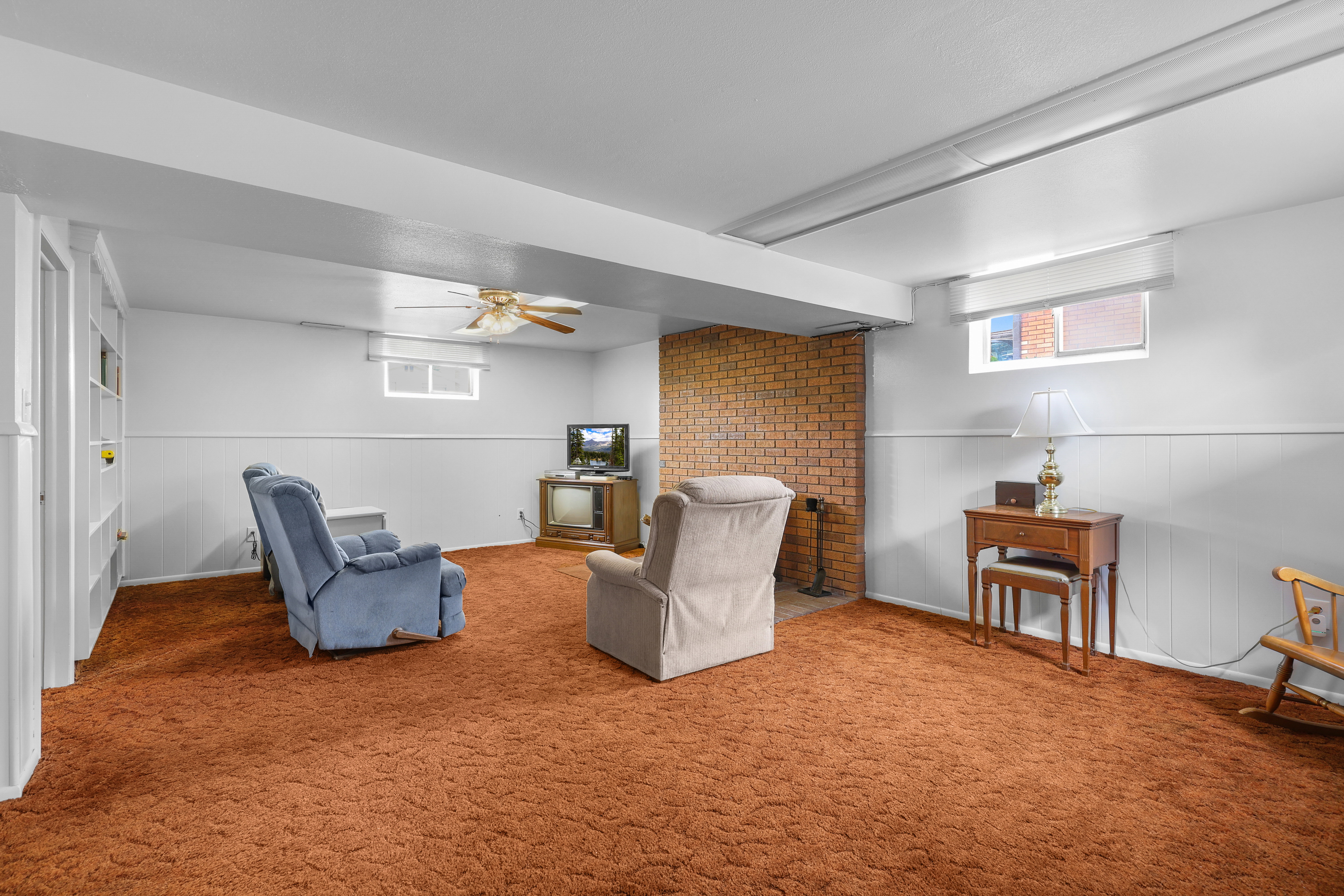Interior living space featuring exposed ceiling beams, white wainscoting, and a brick accent wall with a fireplace