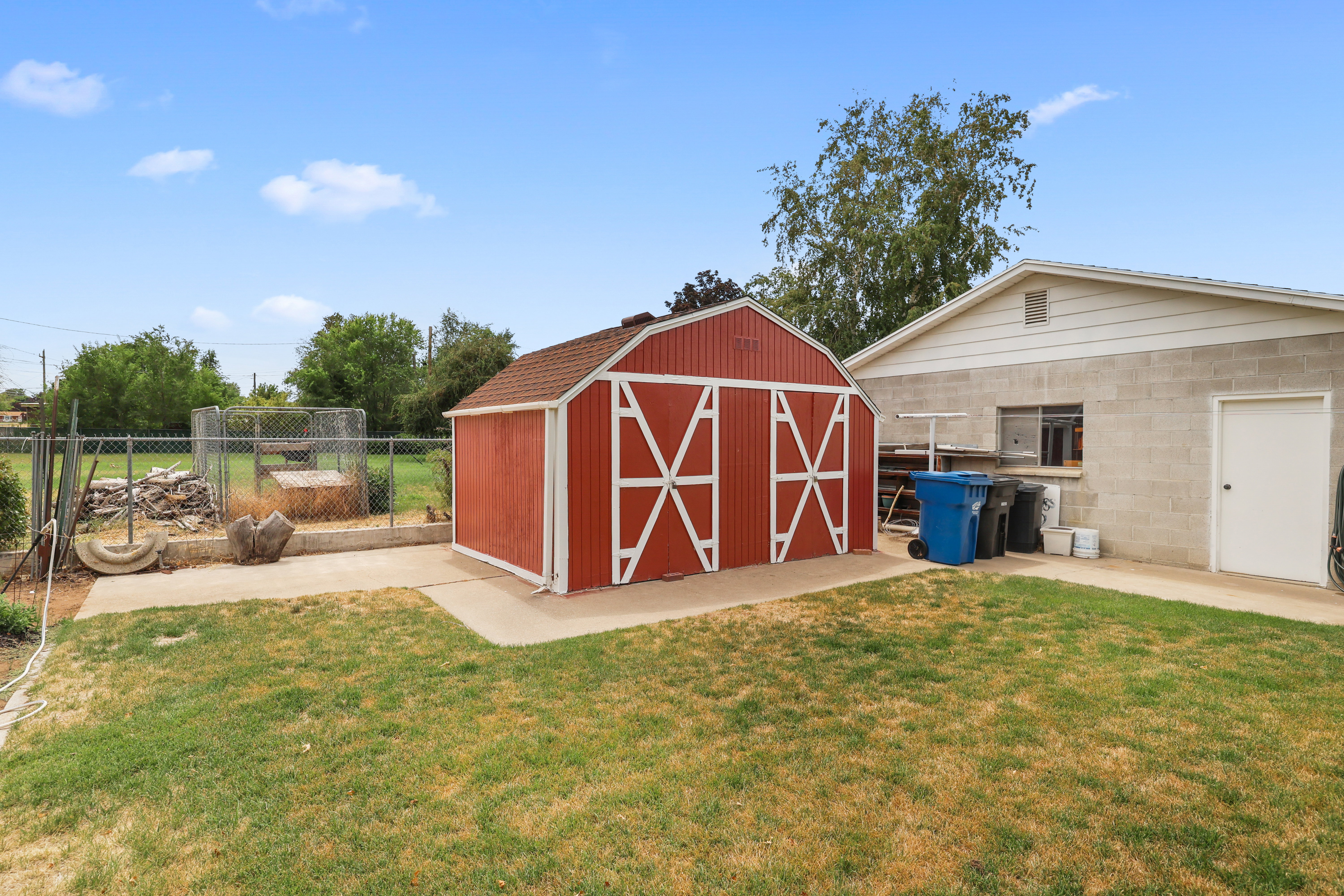 Backyard featuring a red barn-style shed, concrete block utility building, and a chain-link fence